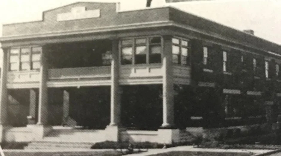 Black and white photo of a two-story residential building with a covered porch and multiple windows.