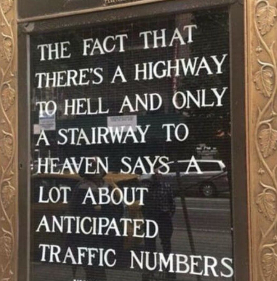 A window with a sign that humorously comments on the traffic and highway system, mentioning a highway to hell, a stairway to heaven, and traffic numbers.