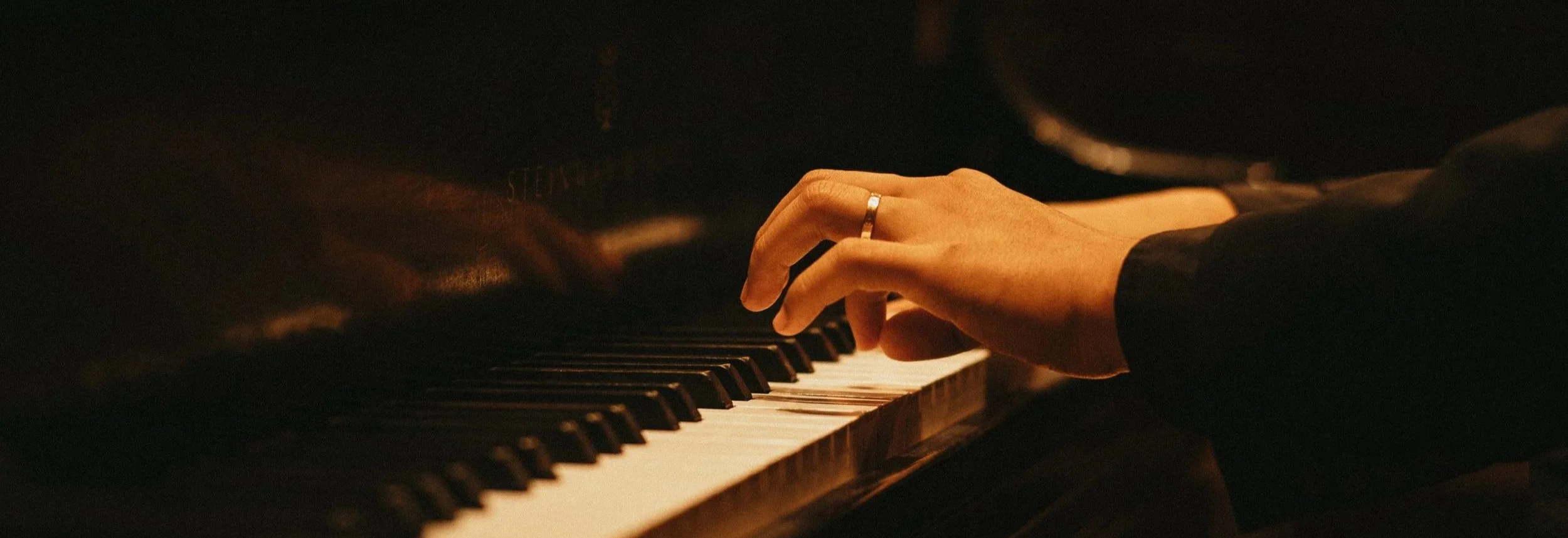 Close-up of a person's hand wearing a ring, playing a piano in a dimly lit setting.