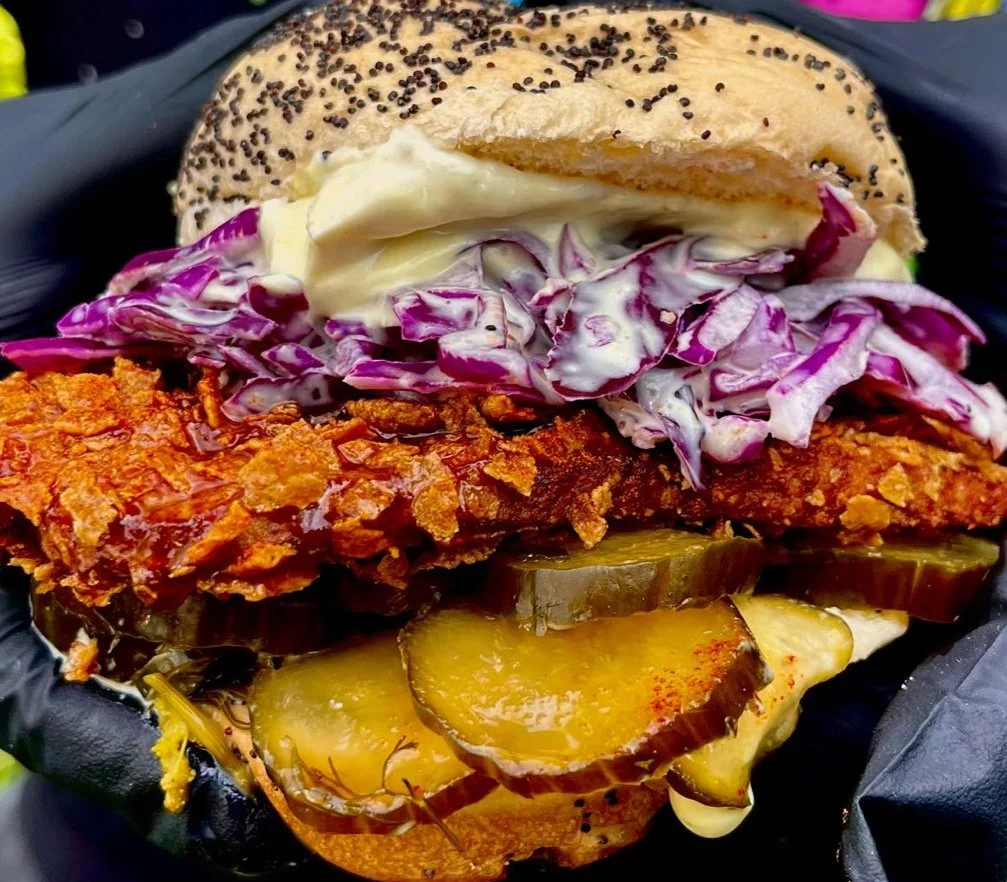 A layered spicy chicken sandwich with mayo, cabbage and pickles on a sesame seed bun