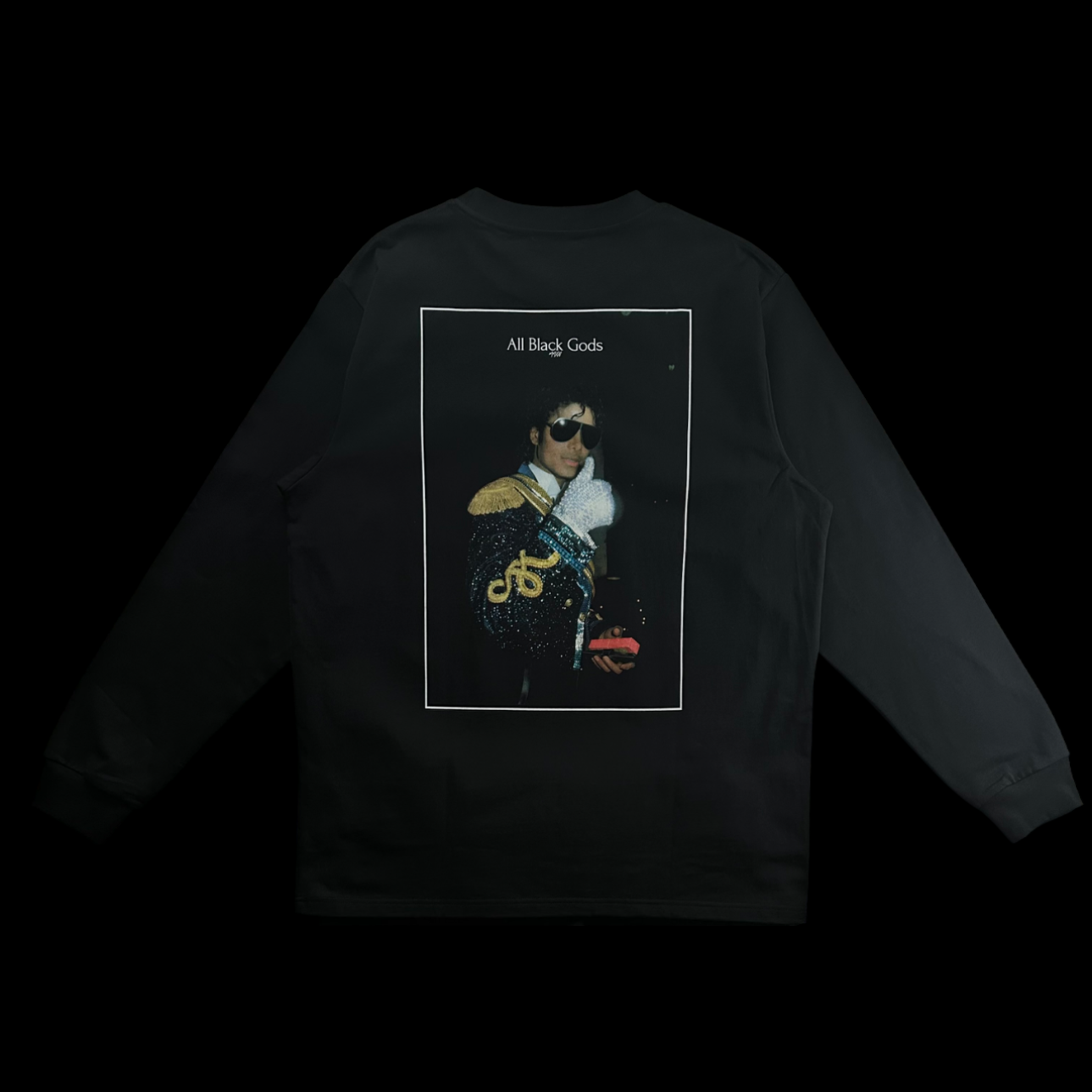Black long-sleeve shirt with a graphic print on the back featuring a person in a sparkly jacket, sunglasses, and a white glove, holding a small object. The text 'All Black Gods' is at the top of the graphic.