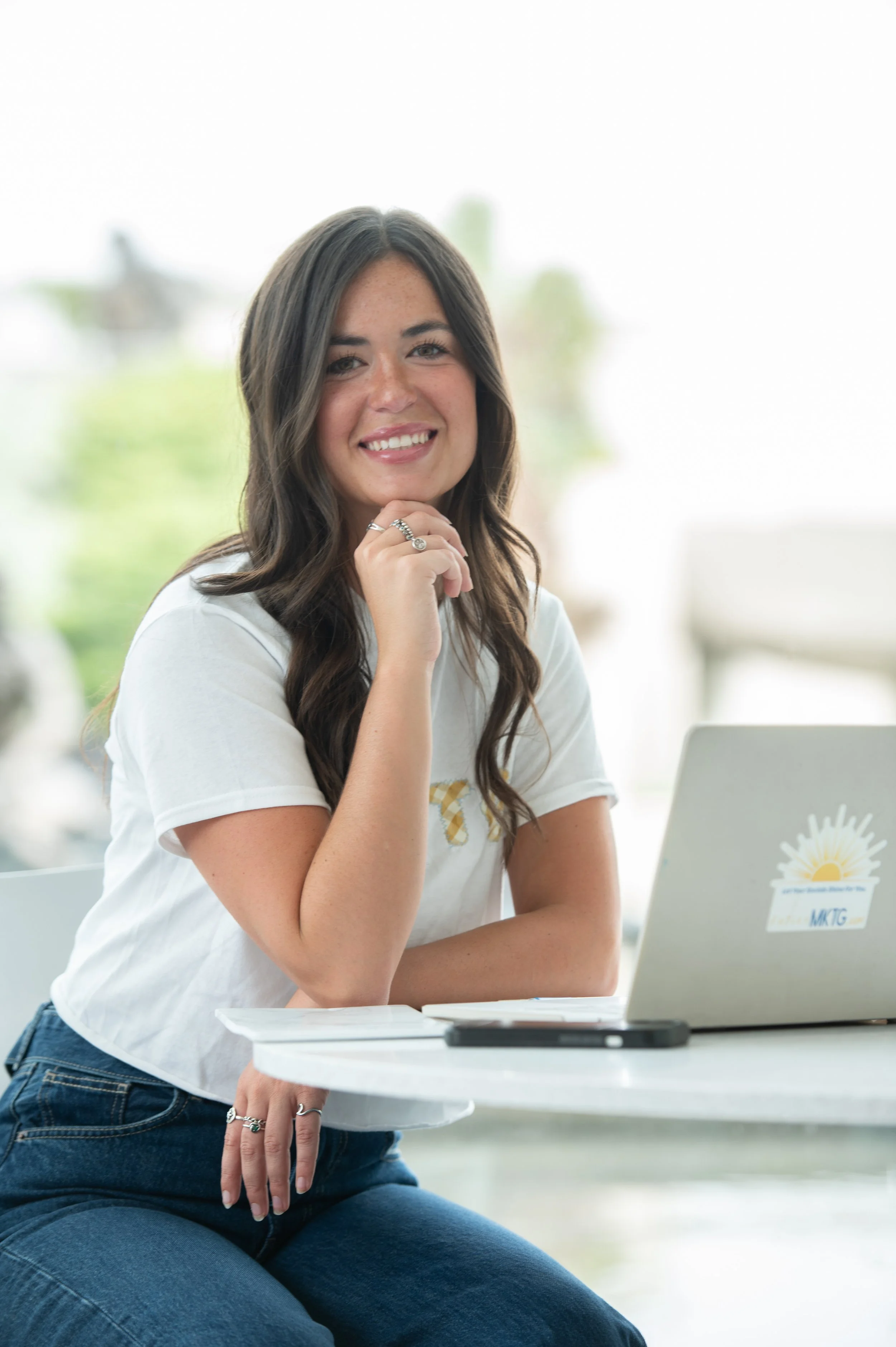 Founder of Katie's MKTG marketing agency, smiling at laptop while managing client marketing strategy
