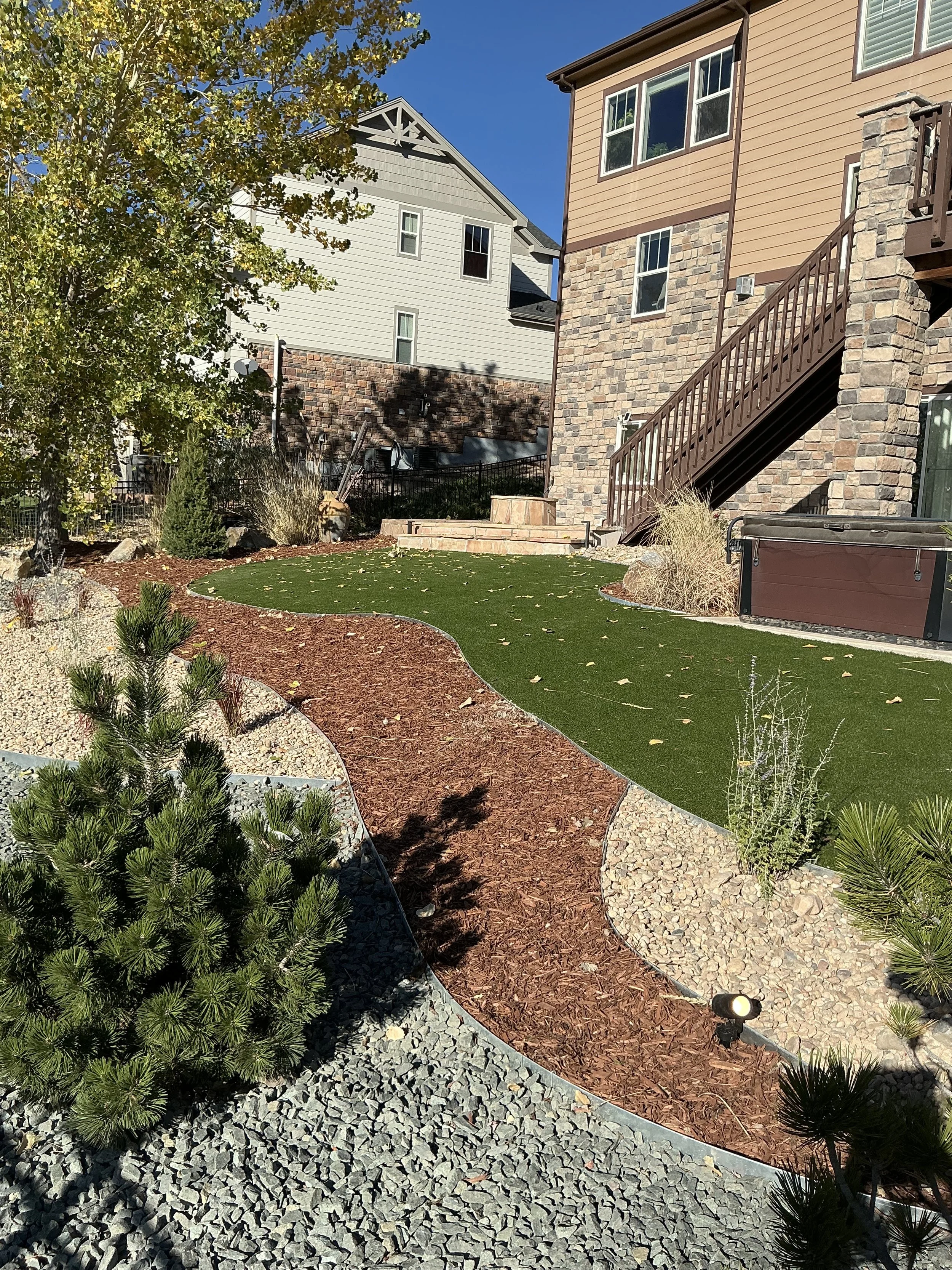 Backyard with landscaped garden, artificial grass, mulch beds, and house with stone and siding exterior