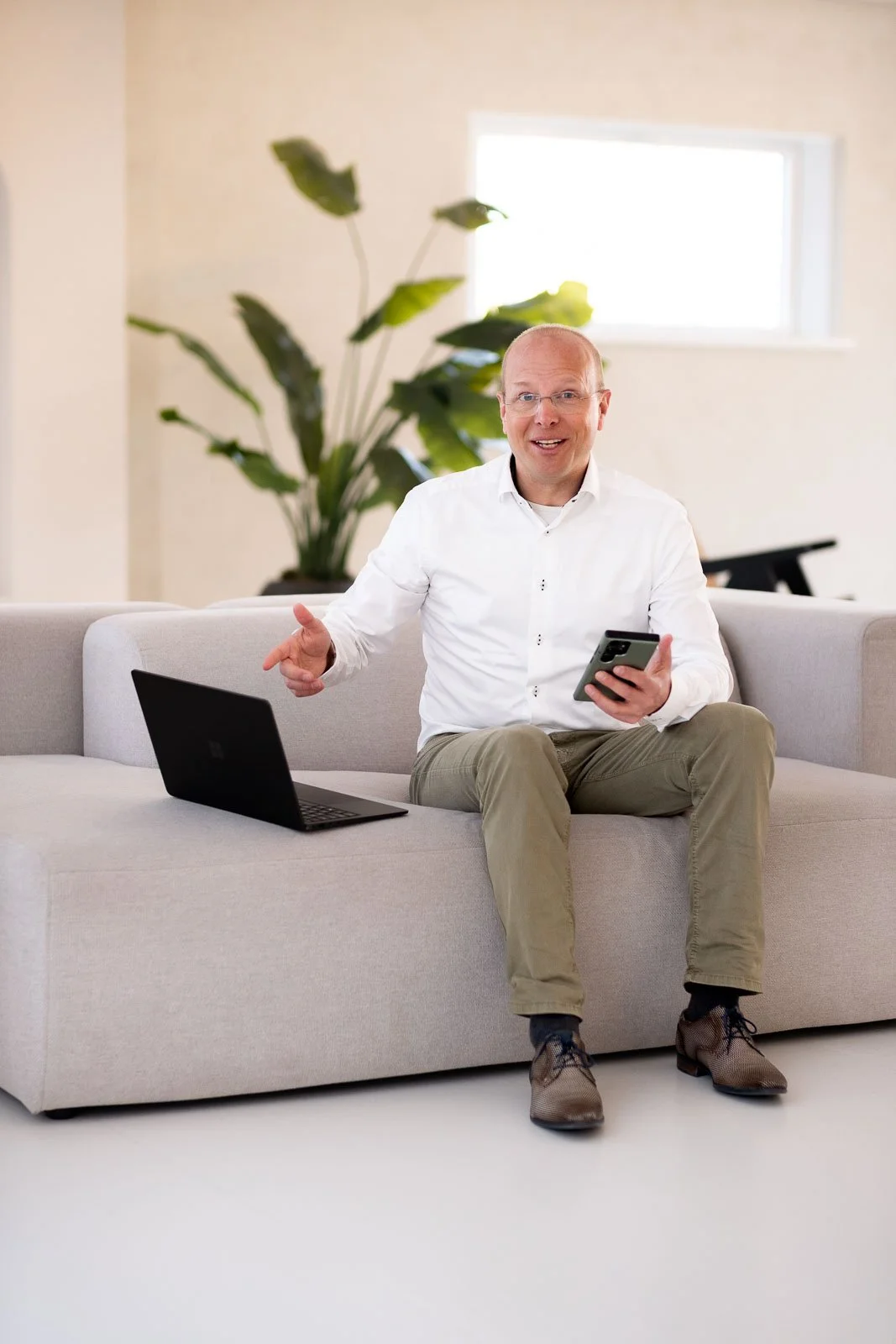 Spontane foto van ondernemer werkend met laptop vanaf bank en met telefoon en laptop