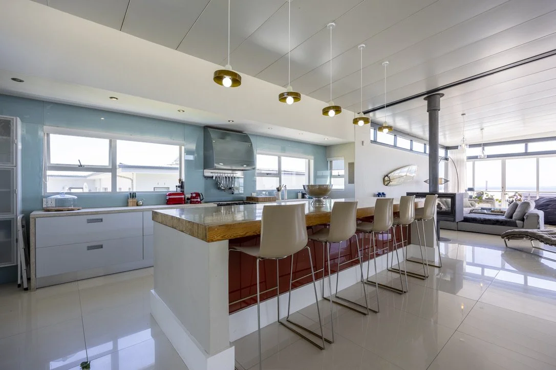 Modern kitchen with a large island, bar stools, and a view of a living room with large windows.