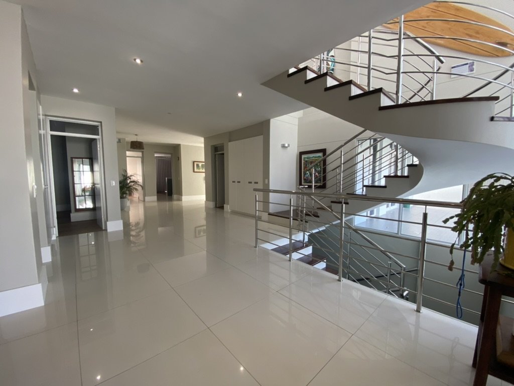 Modern interior of a house with a spiral staircase, large white tiles, and white walls with framed artwork.