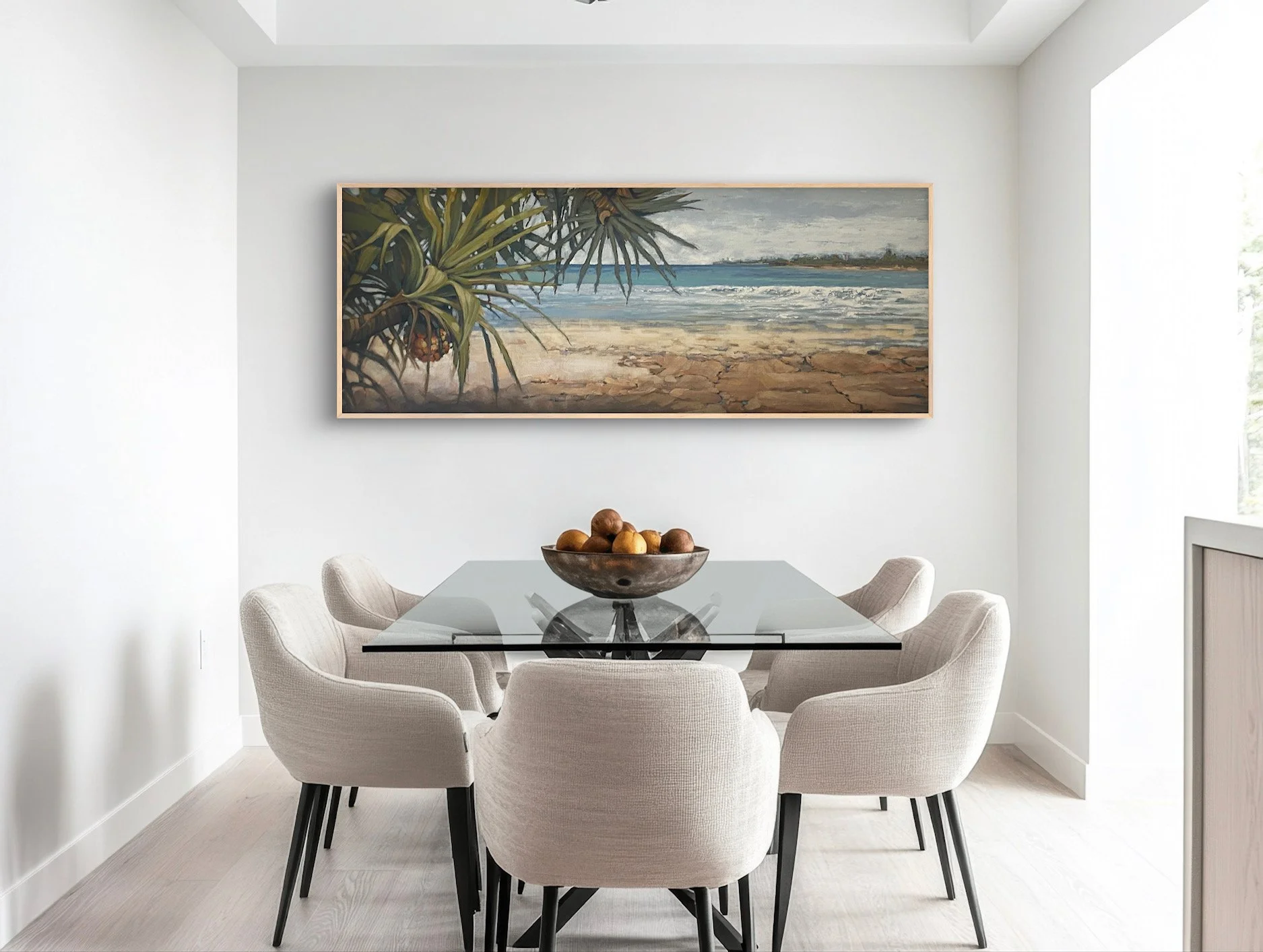 Modern dining room with a glass table, six beige chairs, a bowl of fruit, and a landscape painting of a beach on the wall.