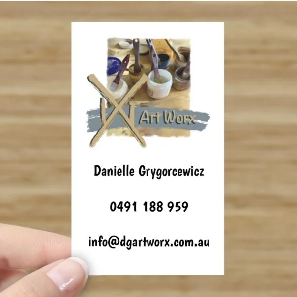 Business card for Danielle Grygorcewicz with art supplies in the background, including paintbrushes and containers of paint.