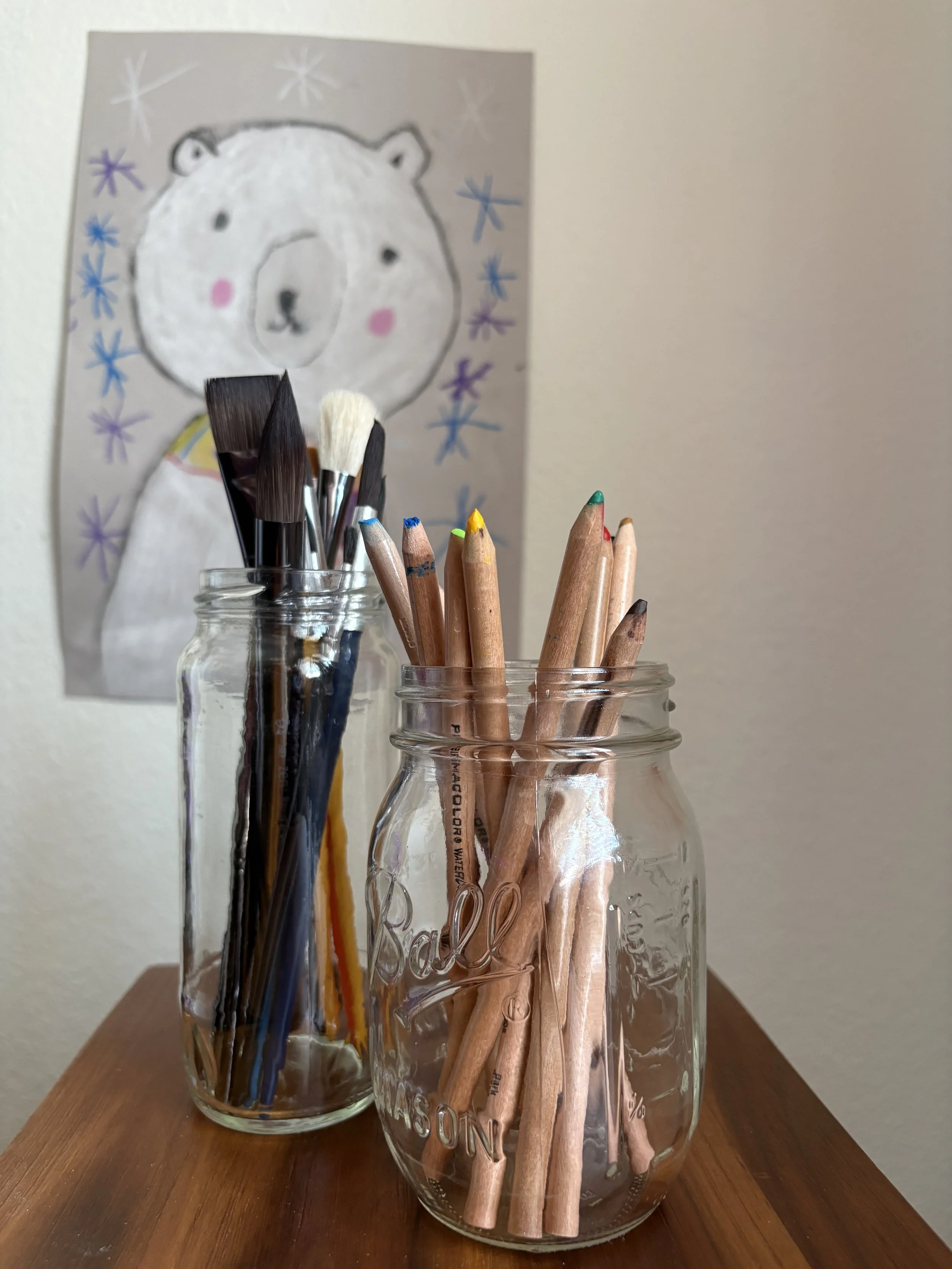 Glass jars filled with paintbrushes and watercolor pencils