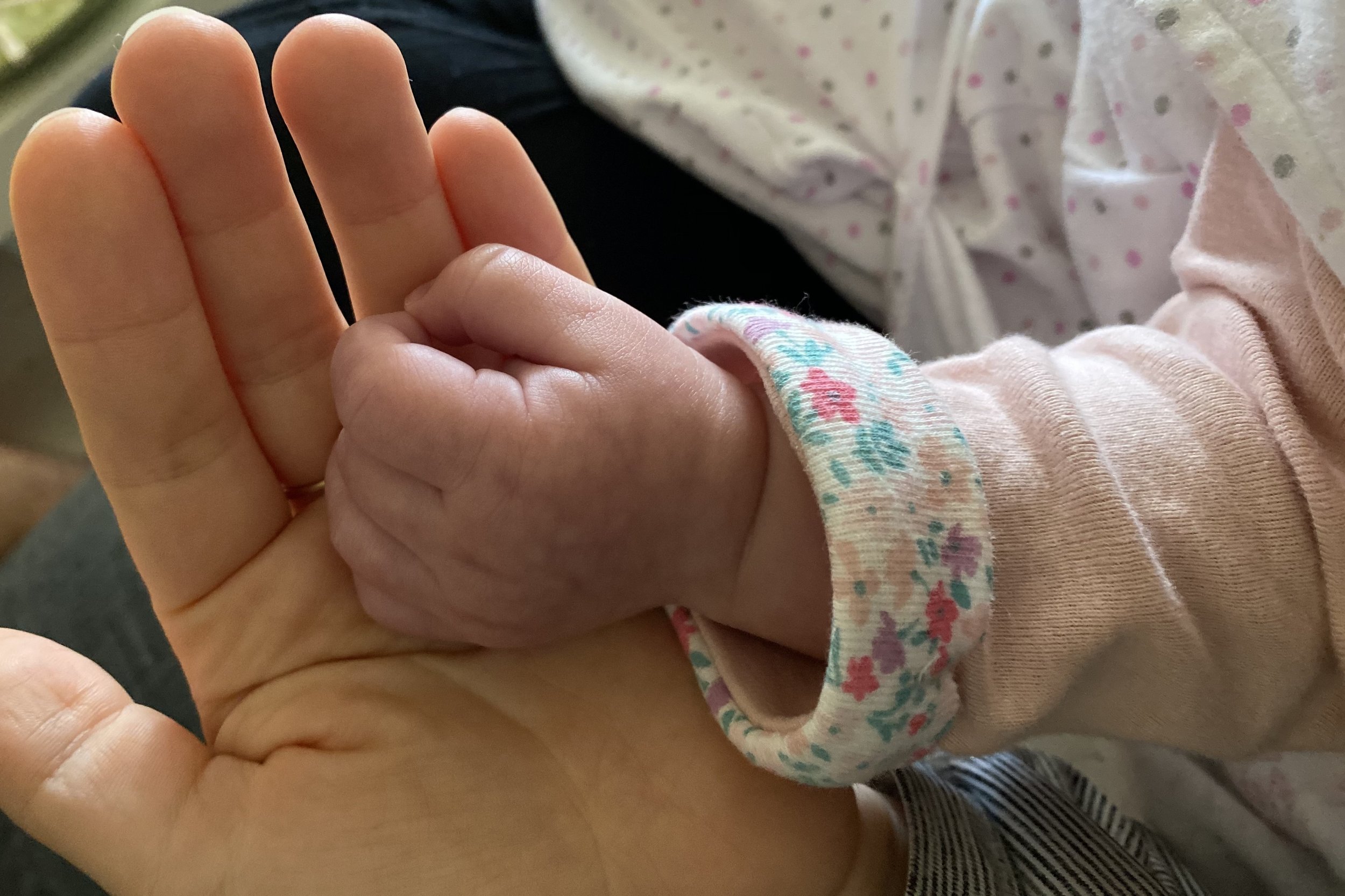 A mother's open hand gently holding a baby's tiny hand.