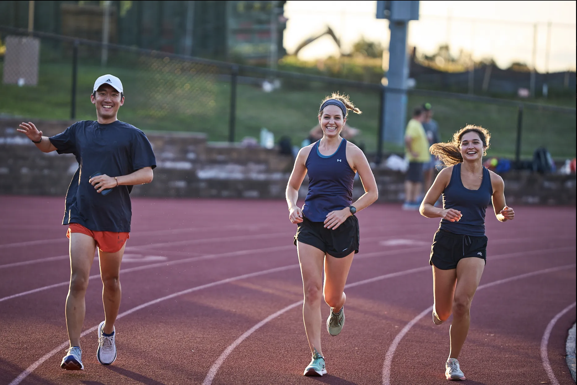 Three people running on a track during sunset, smiling and enjoying the exercise.