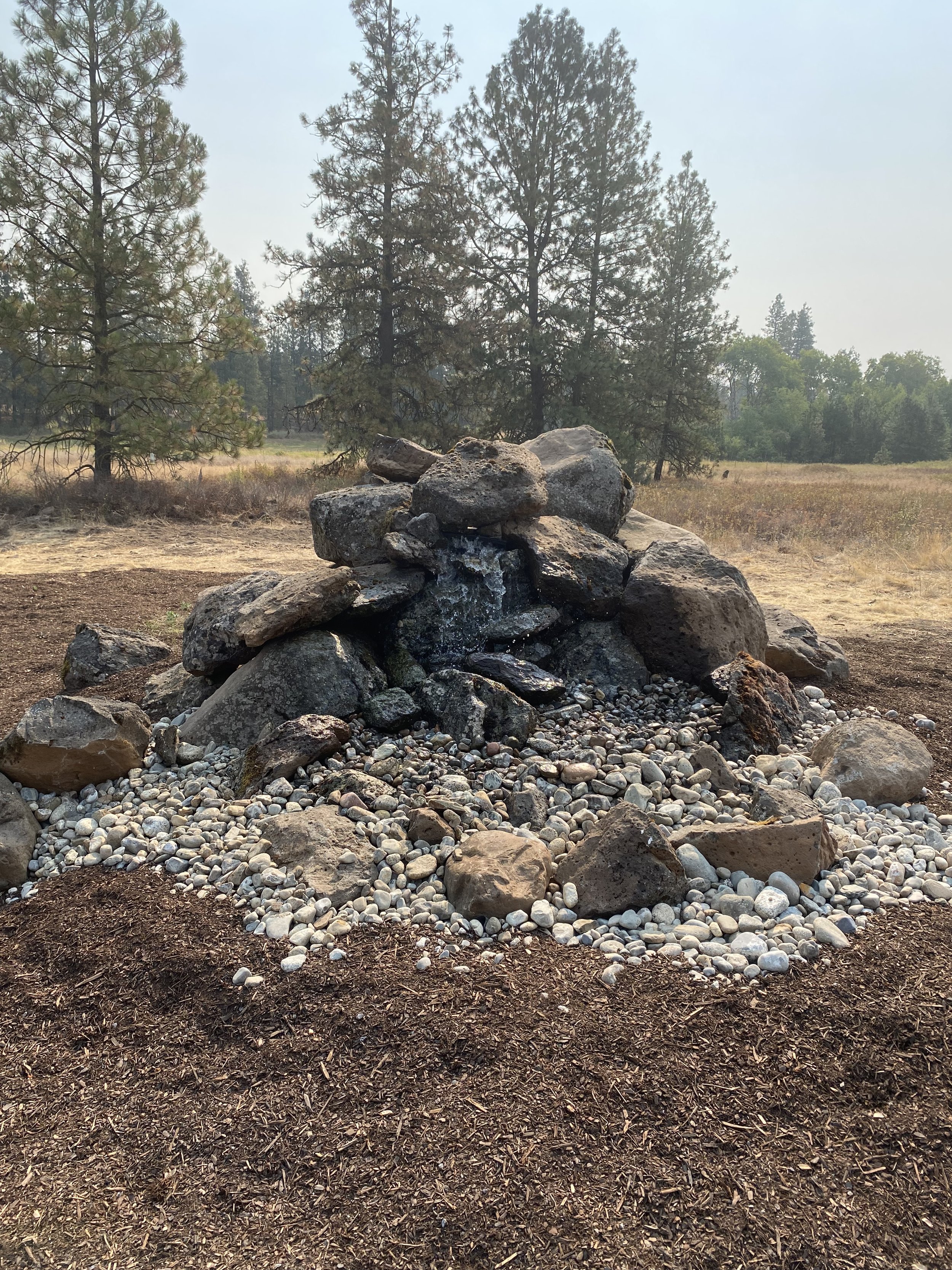 Rock pile with small water feature in natural setting, surrounded by pine trees and dry grassland. Cheney Washington.
