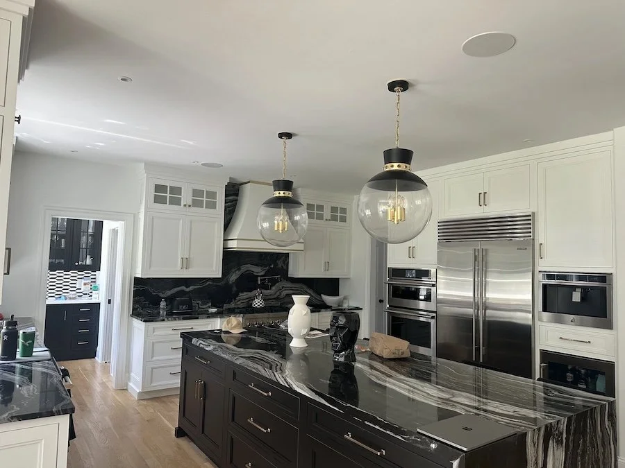 Luxury kitchen featuring in-ceiling speakers, pendant lighting, black marble countertops, and built-in appliances.
