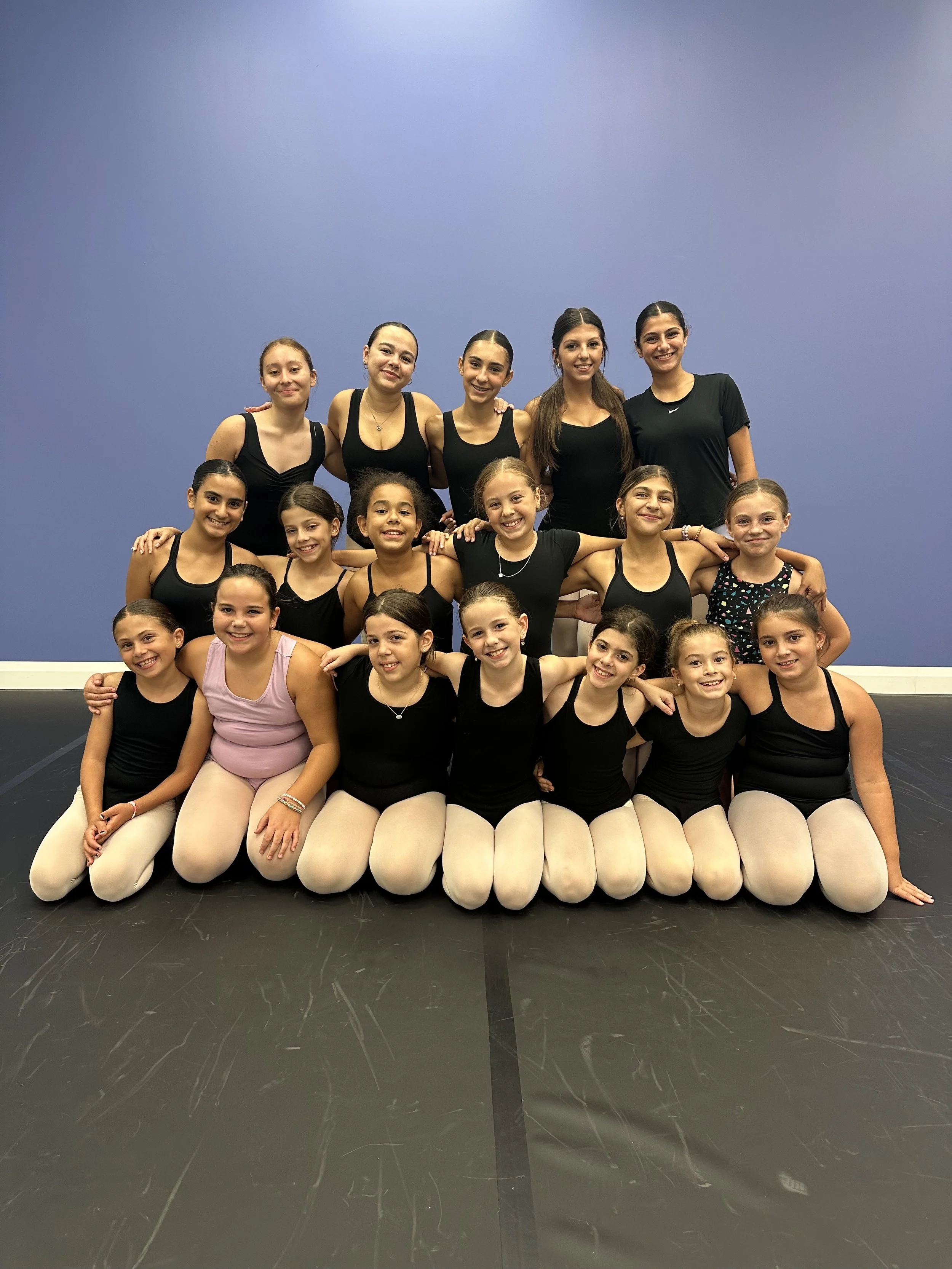 A ballet dancer practicing on stage with arms raised, wearing a white tutu and puffed sleeves, illuminated by stage light.