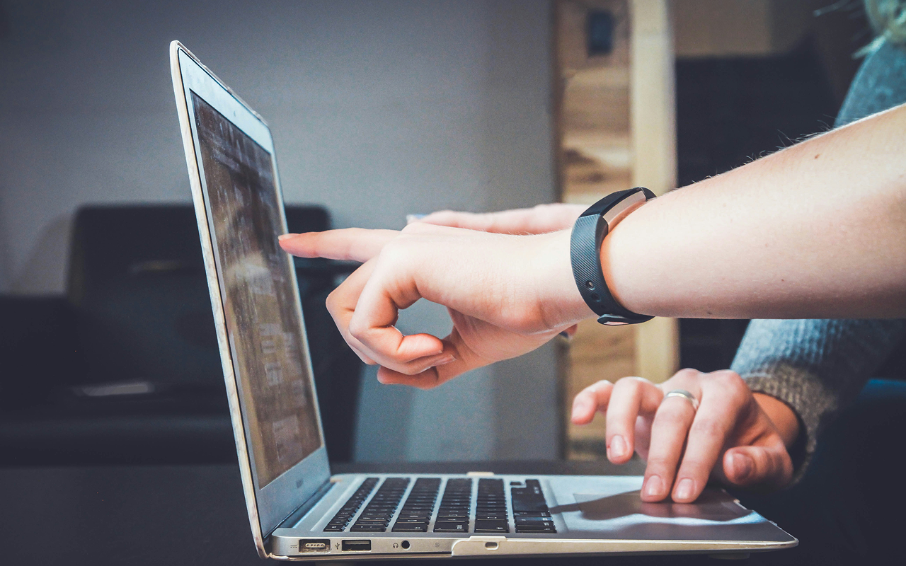 Two people pointing at the same laptop screen, collaborating side by side