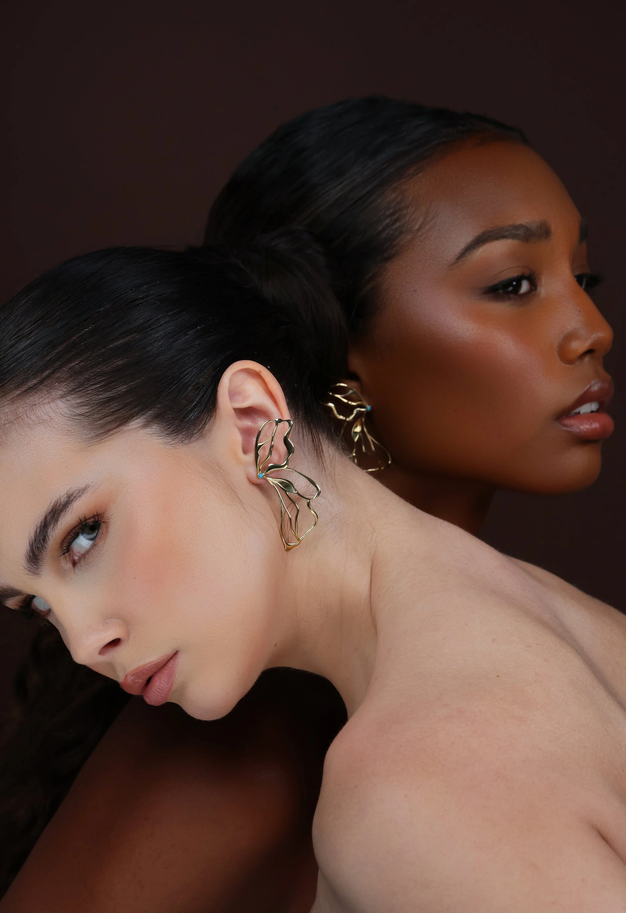 Editorial portrait of two models wearing HANAUREUM Hana earrings, sculptural butterfly-inspired designs in 14K gold with signature turquoise details.