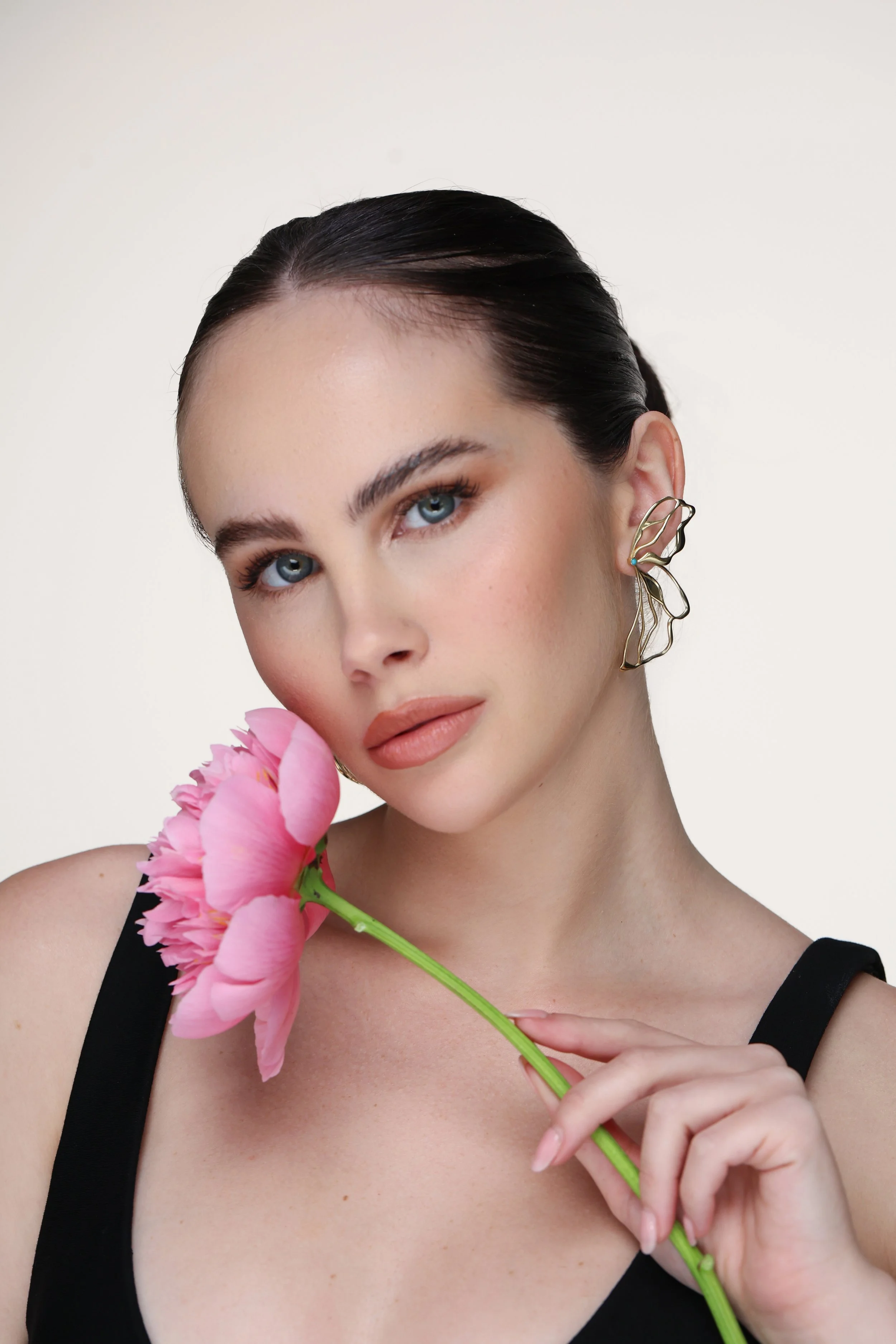 Editorial portrait of a model holding pink flowers and wearing the Hana 14K gold butterfly earring with a turquoise accent