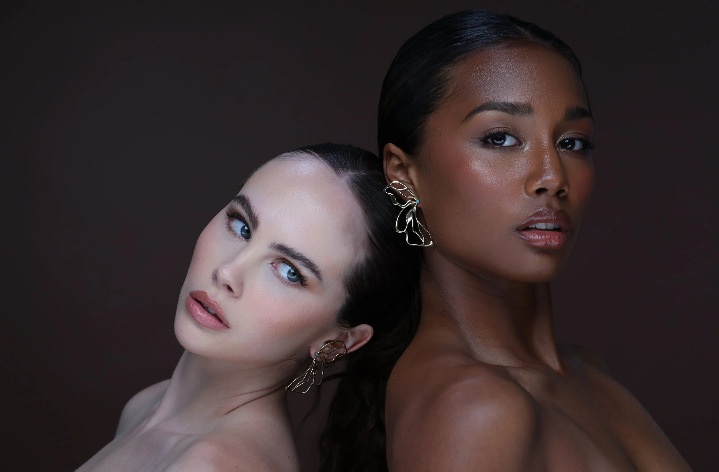 Close-up editorial portrait of two models wearing Hana 14K gold butterfly earrings with turquoise accents