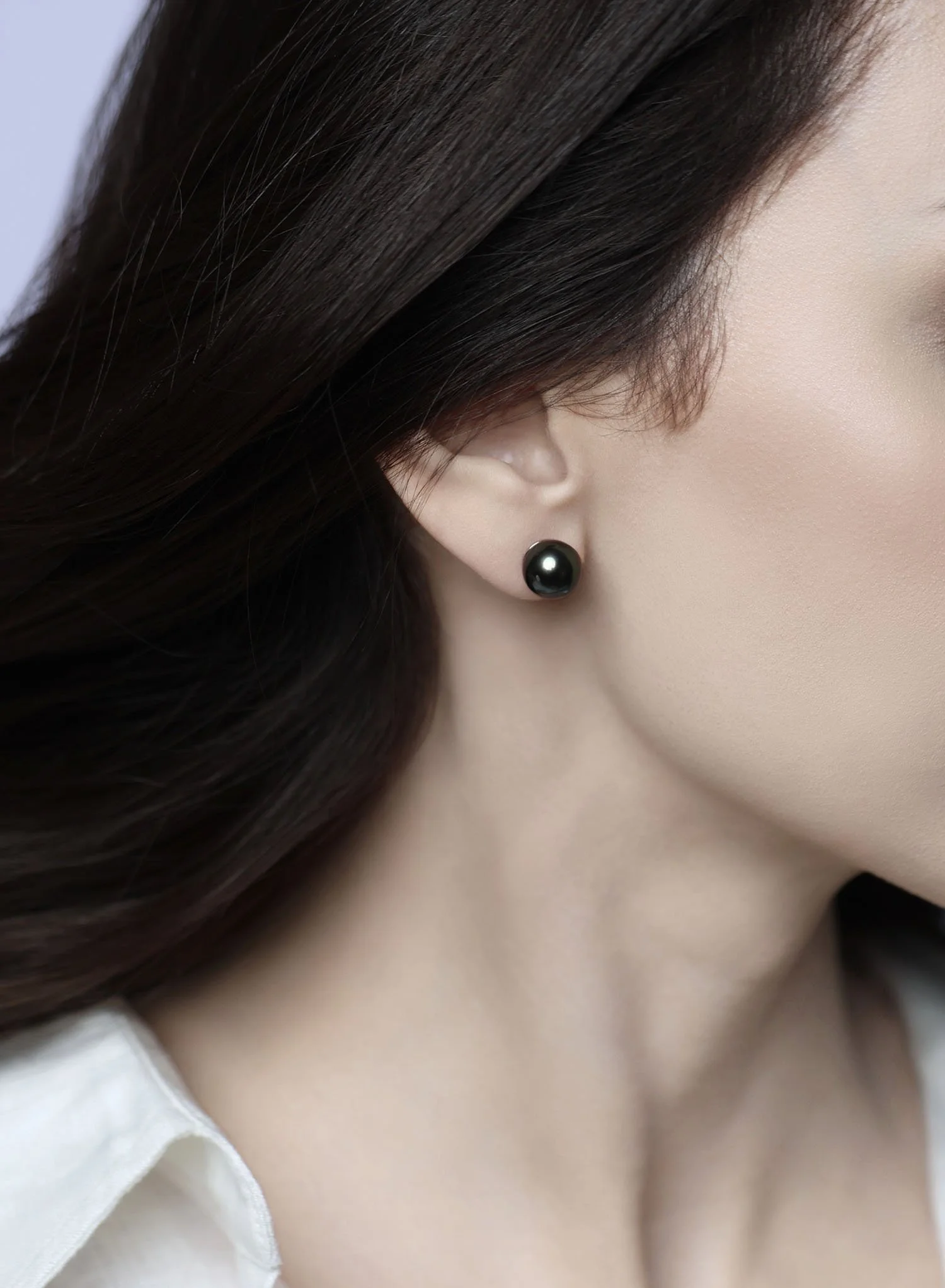 Close-up side profile of a model wearing the Noire dark Tahitian pearl stud earring crafted in 14K white gold