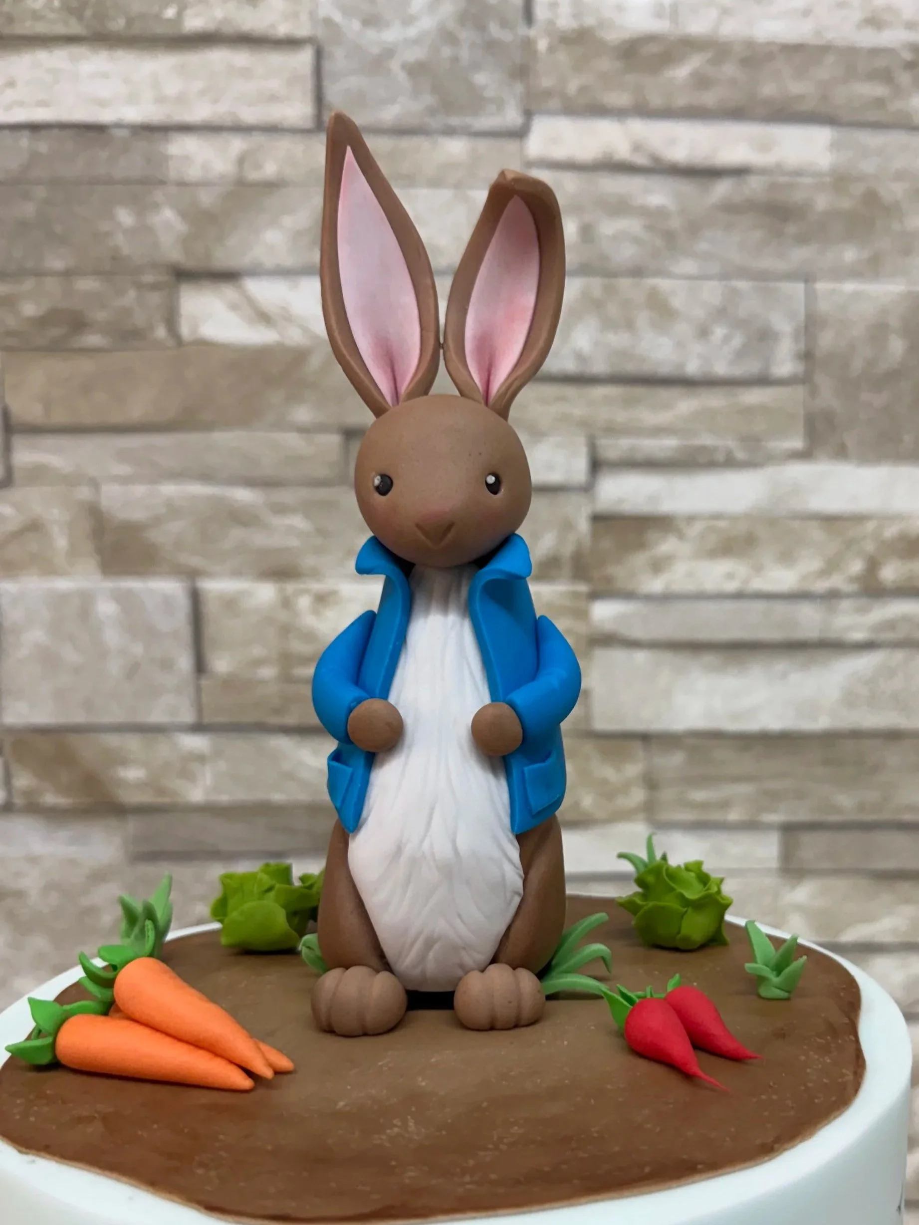 Peter Rabbit cake figurine with radish, carrots, lettuce and grass around his feet