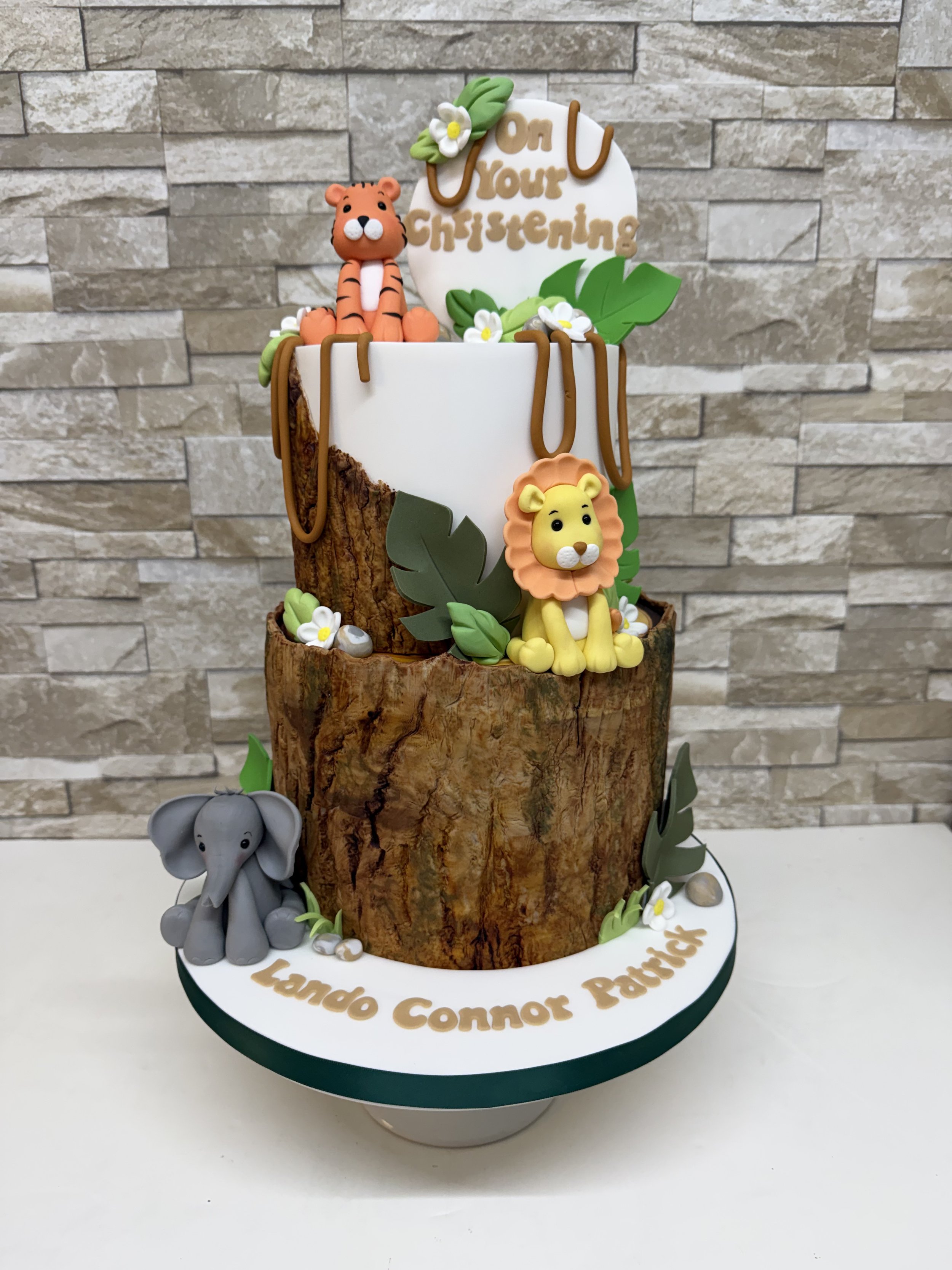 Two tier birthday cake with a jungle theme. Log tier, with Tiger, Lion and Elephant sugar fingurines