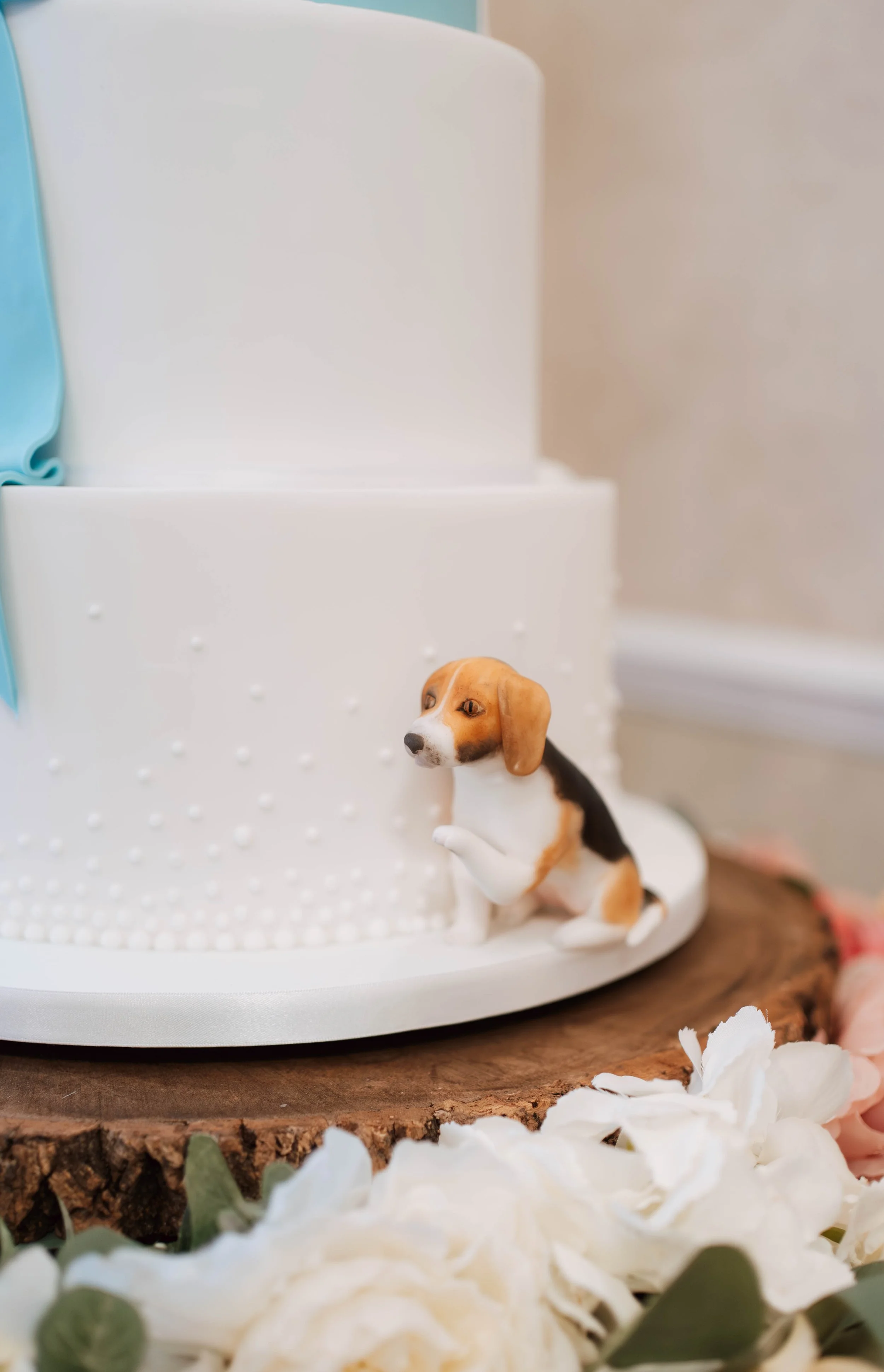 Beagle dog cake figurine with paw lifted, sat at the bottom of a white wedding cake