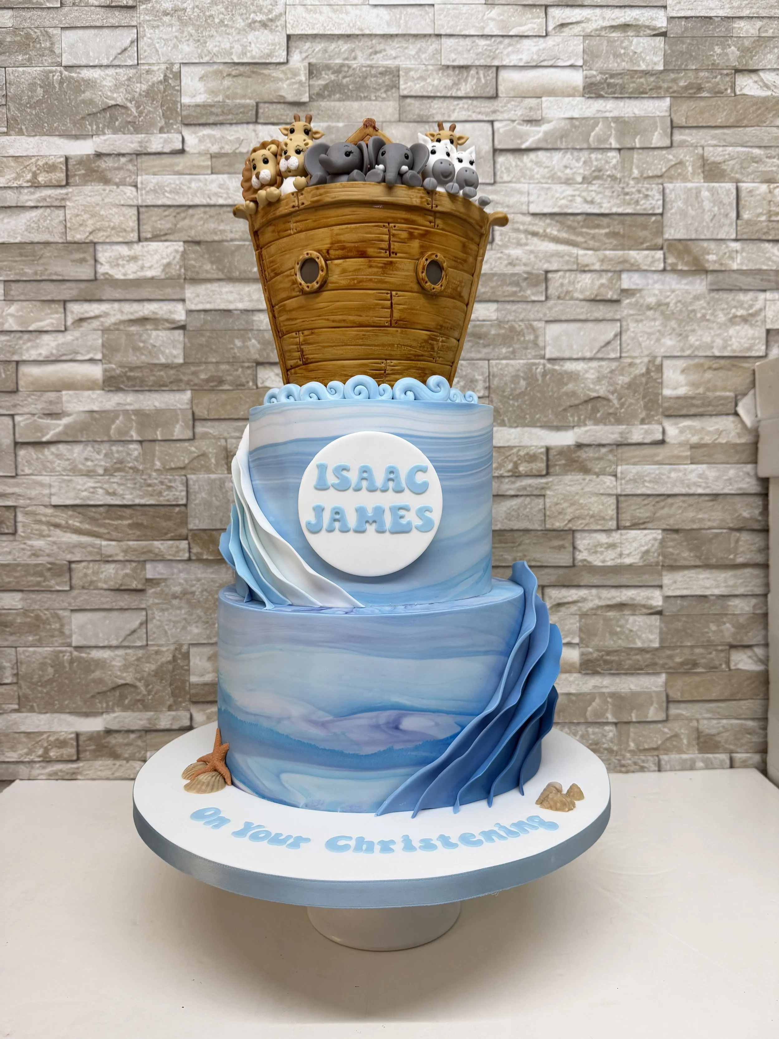 3 tier Christening cake with a Noah's Ark theme. Bottom tiers as 'sea' with top tier the Ark with sugar craft animals inside