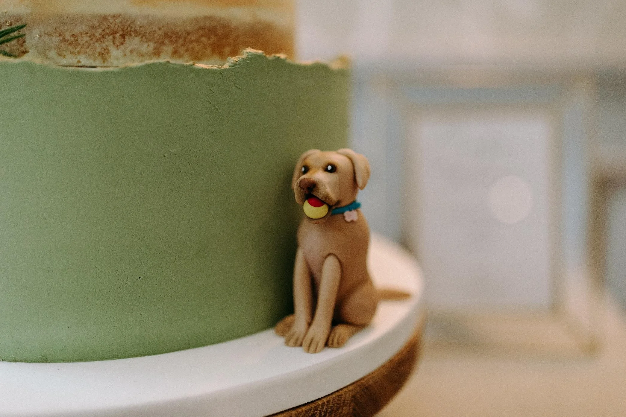 Labrador dog cake figurine at the side of a green buttercream wedding cake