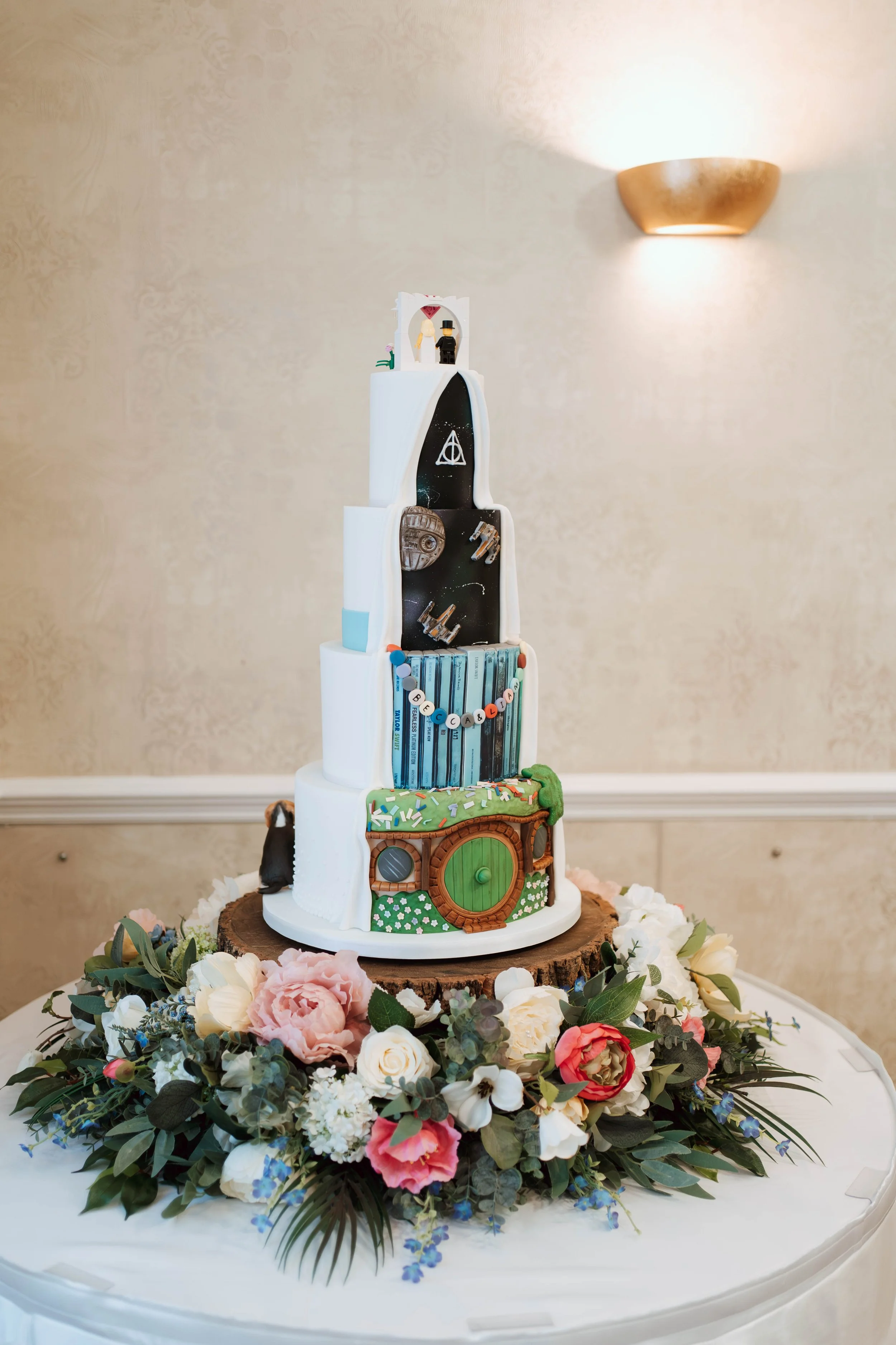 Back side of a reveal wedding cake, consisting of the Hobbit, space, and music theme placed on a flower cake stand