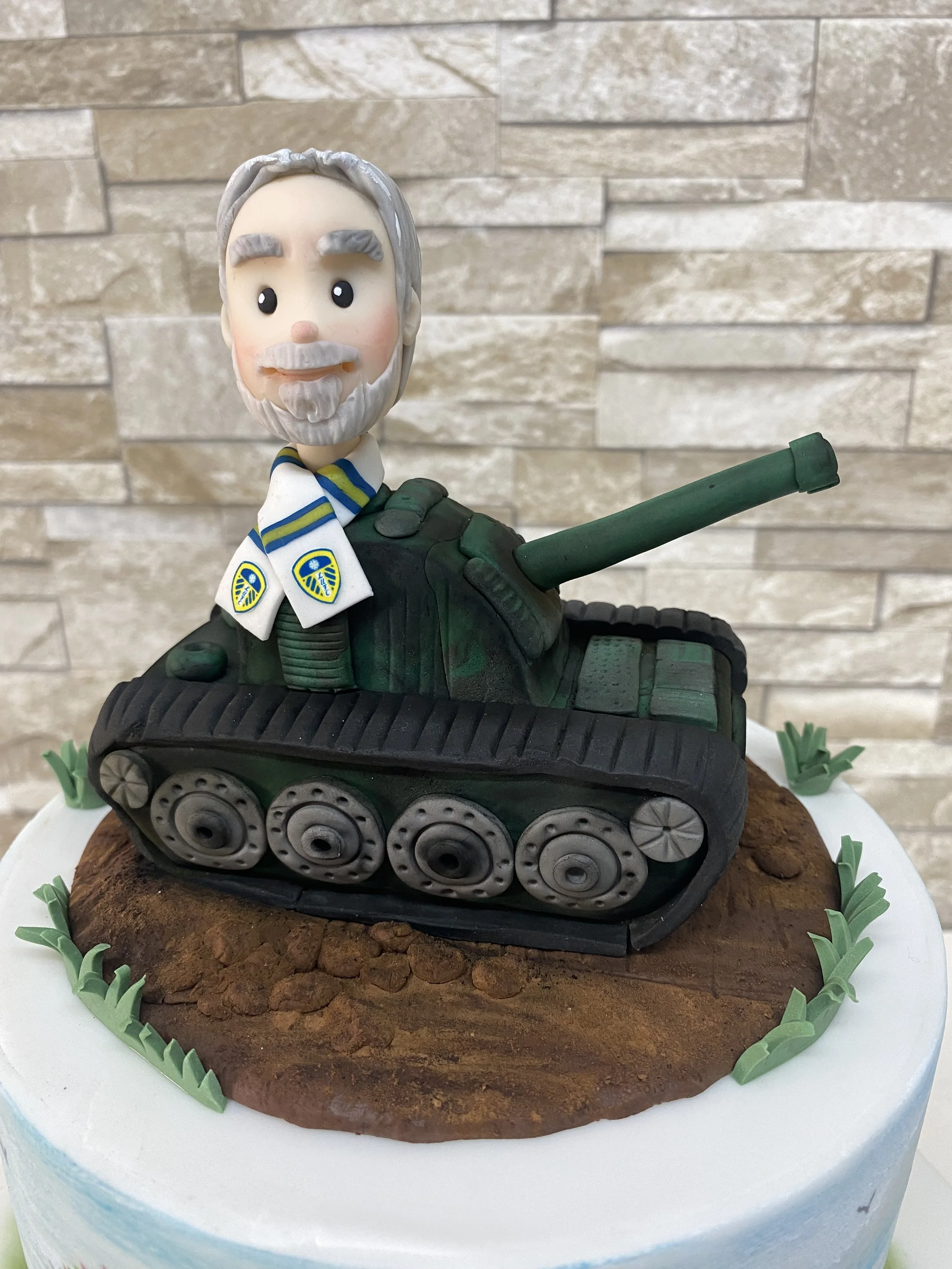 Army tank cake topper with oversized male head coming out of the top, Leeds United scarf around his neck