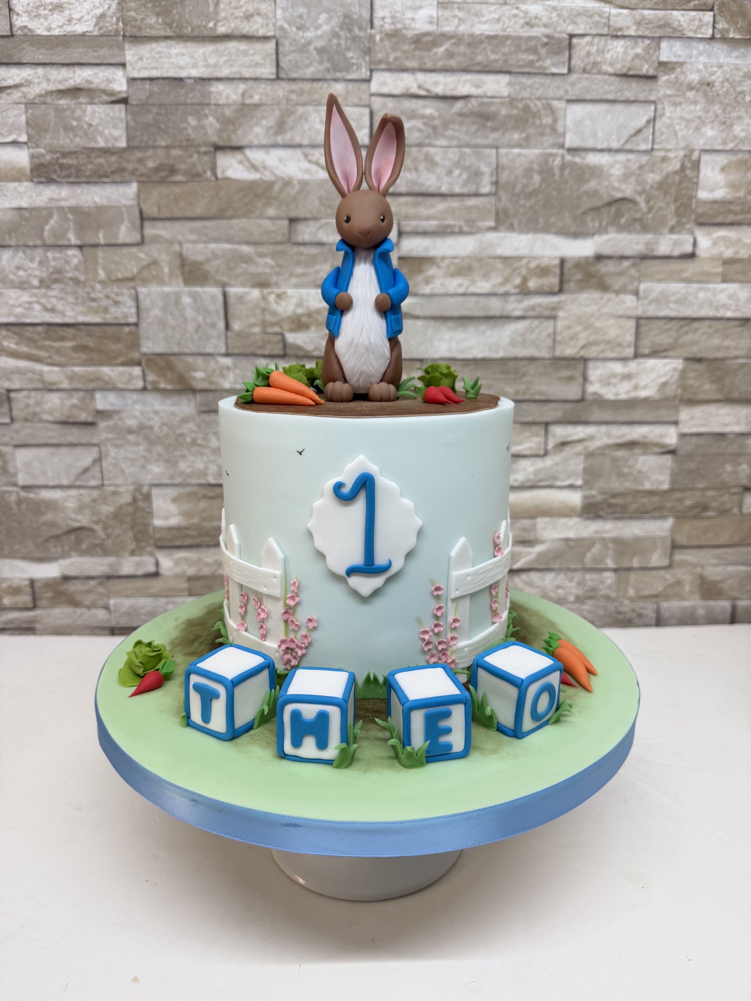 Single tier 1st birthday cake with a Peter Rabbit theme. Peter figurine on top with name blocks at the bottom