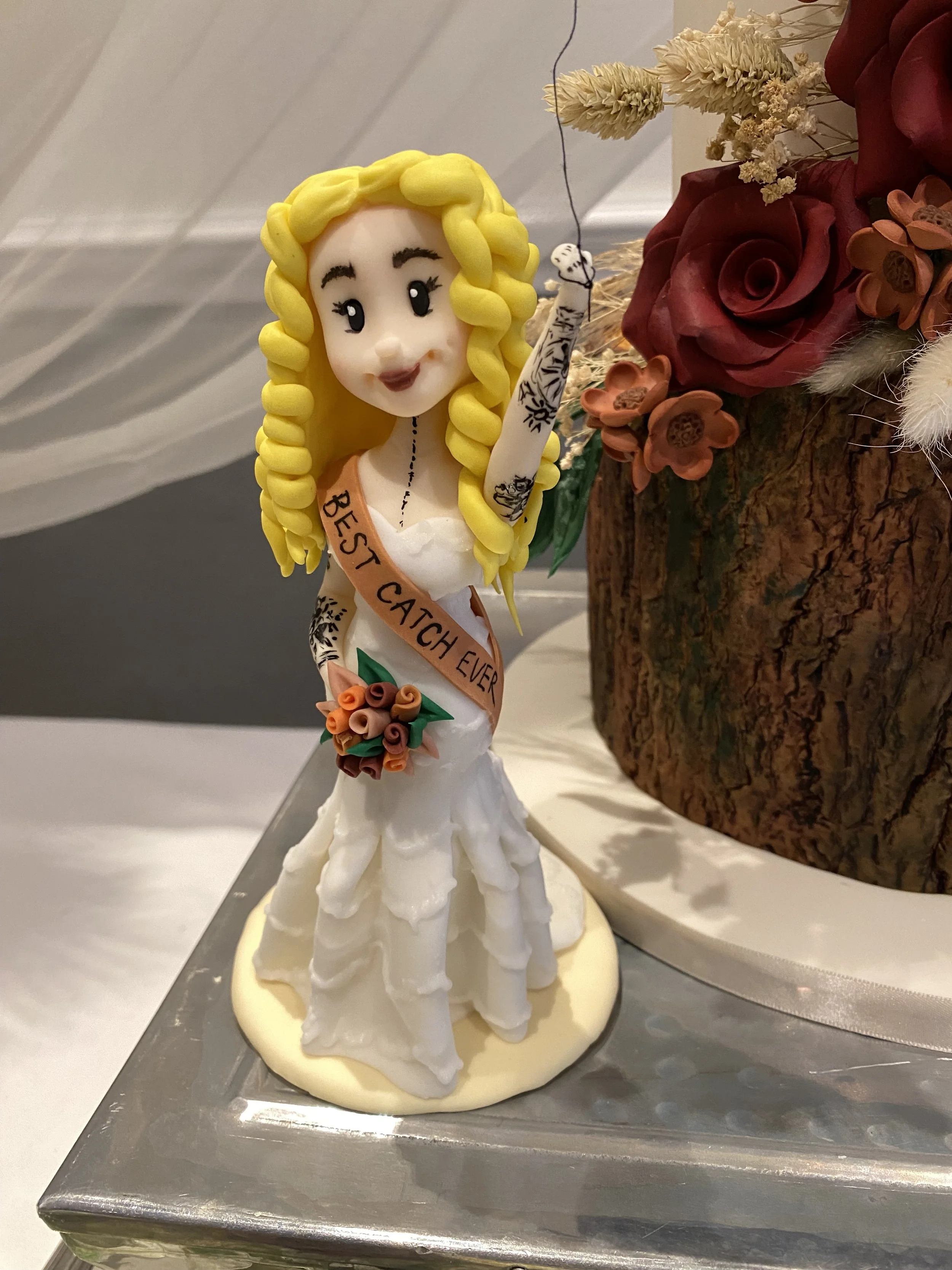Bride figurine with shoulder sash reading 'best catch ever' in a pose like she has been caught with a fishing line