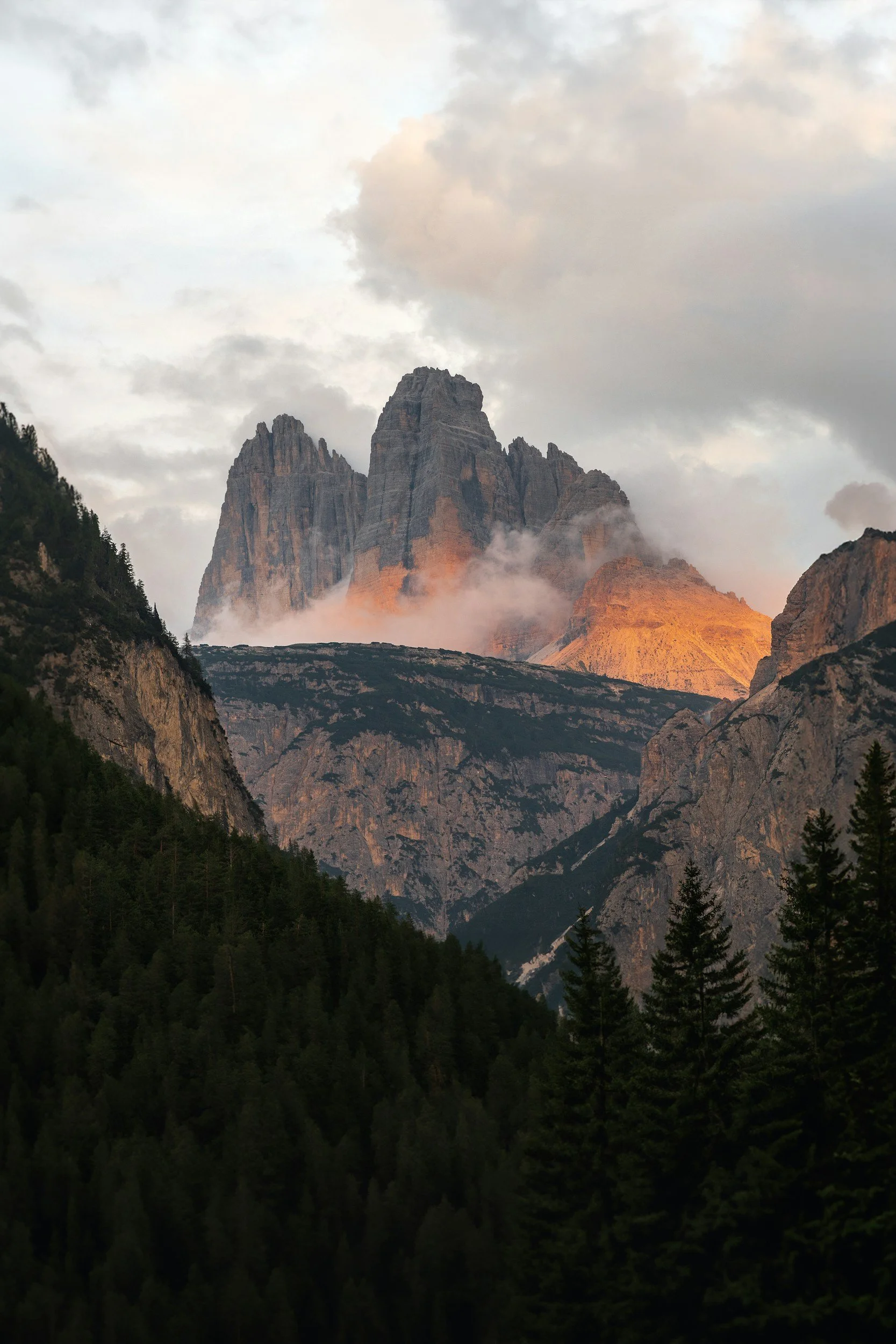 Sunlight illuminating mountain peaks with clouds and forested slopes below.