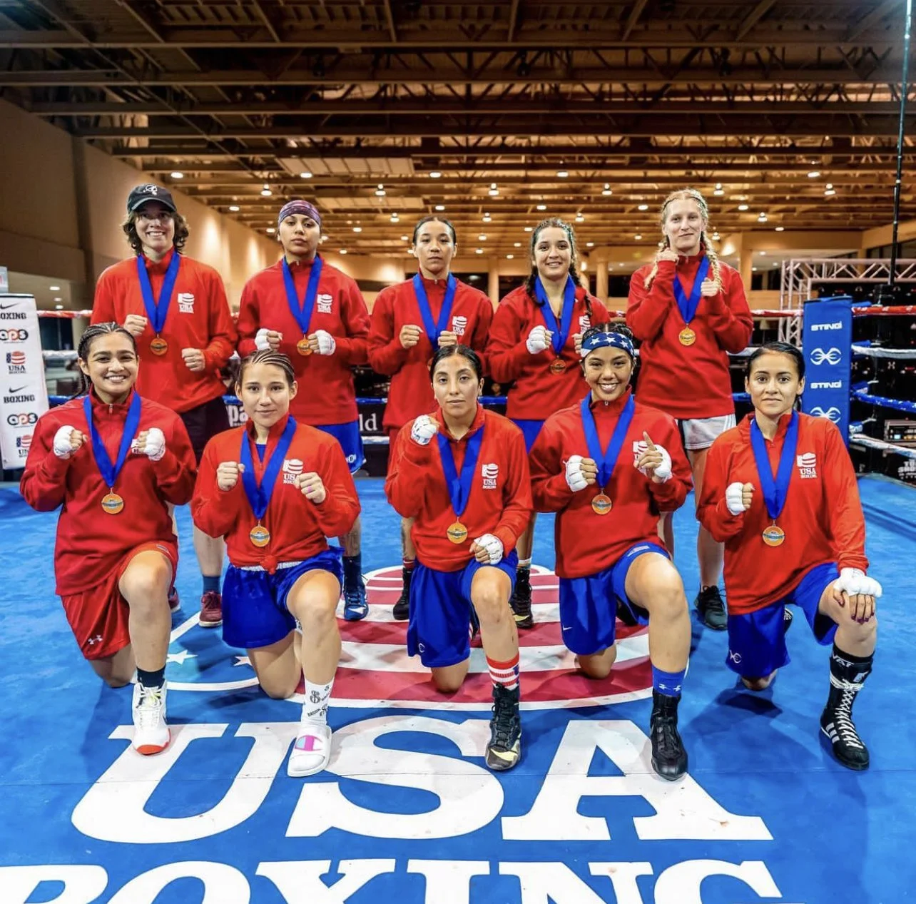 A women's boxing team from the USA posing with medals inside a boxing ring.