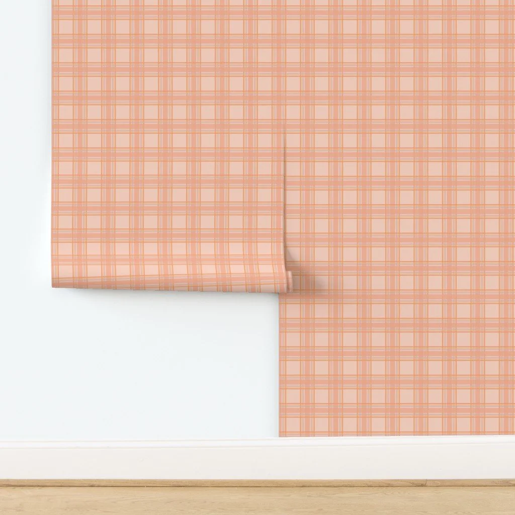 Corner of a wall with peach and cream plaid wallpaper, white baseboard, and wooden floor.