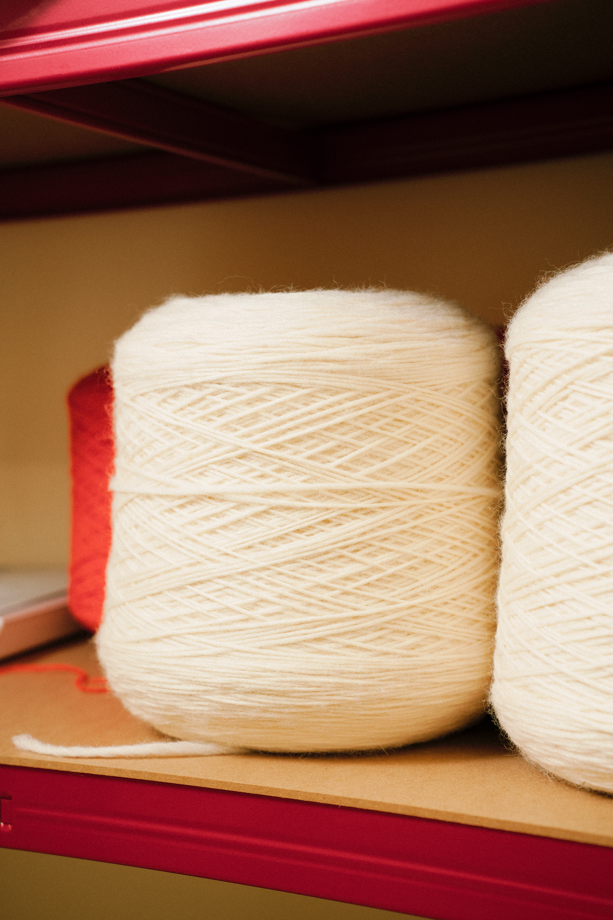 Close-up of two large spools of white yarn on a pink shelf.