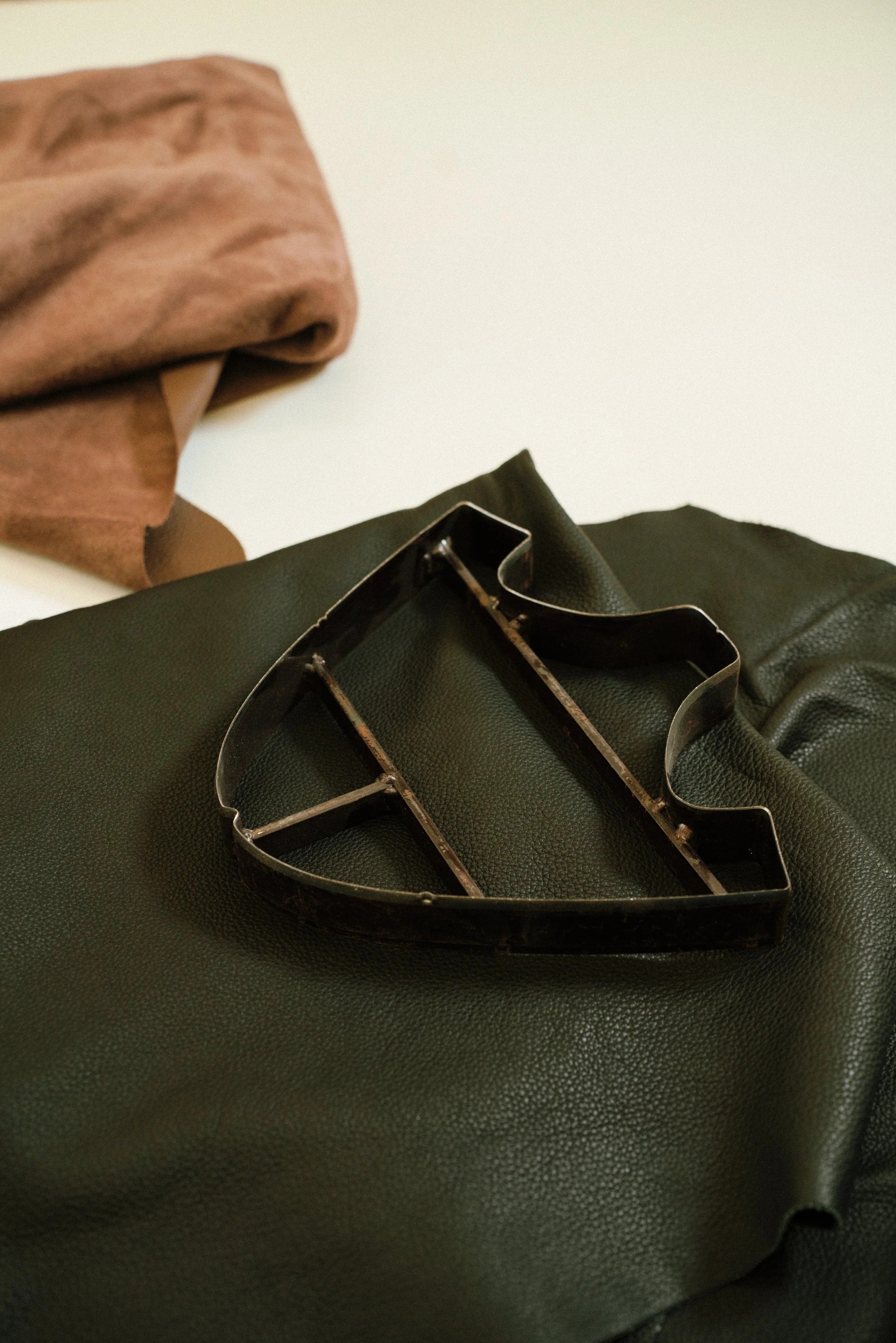 A black metal Superman logo cookie cutter resting on a dark green textured material, with a light brown cloth folded in the background.