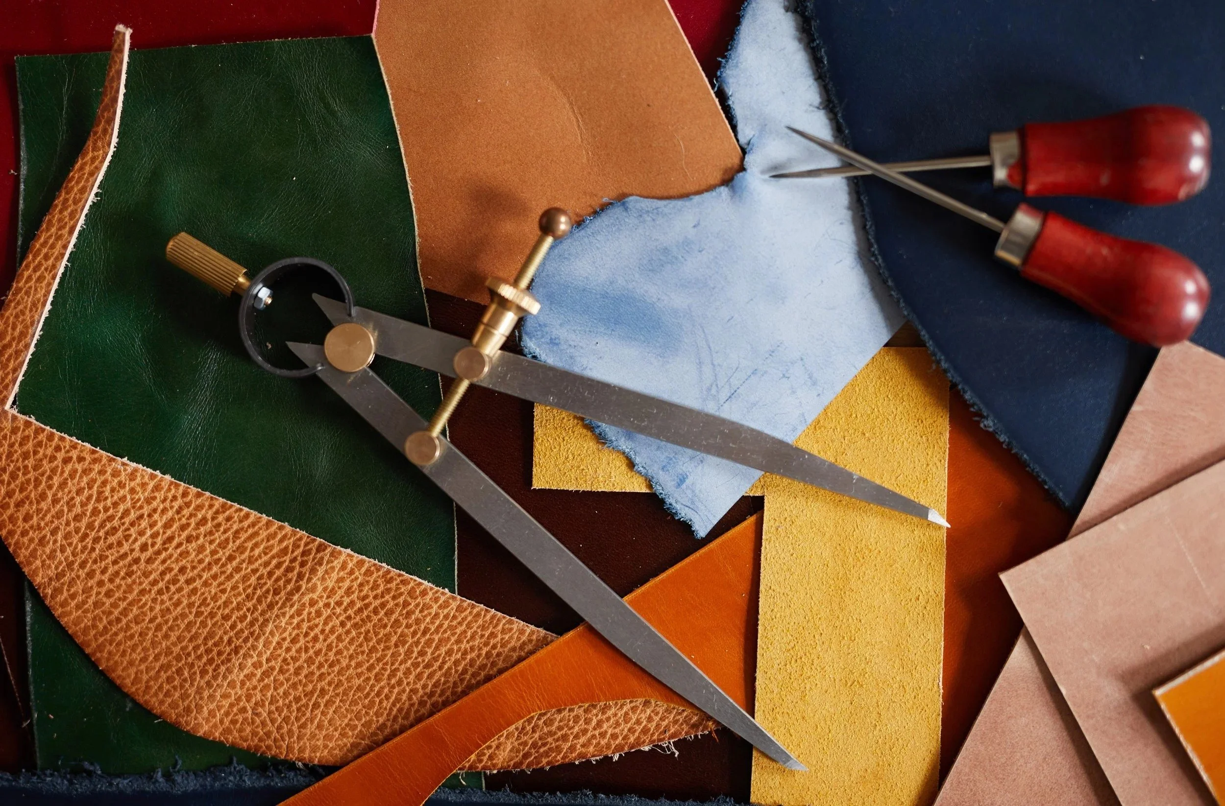 Various colorful leather and suede fabric swatches and a metal compass tool with red handles lying on top.