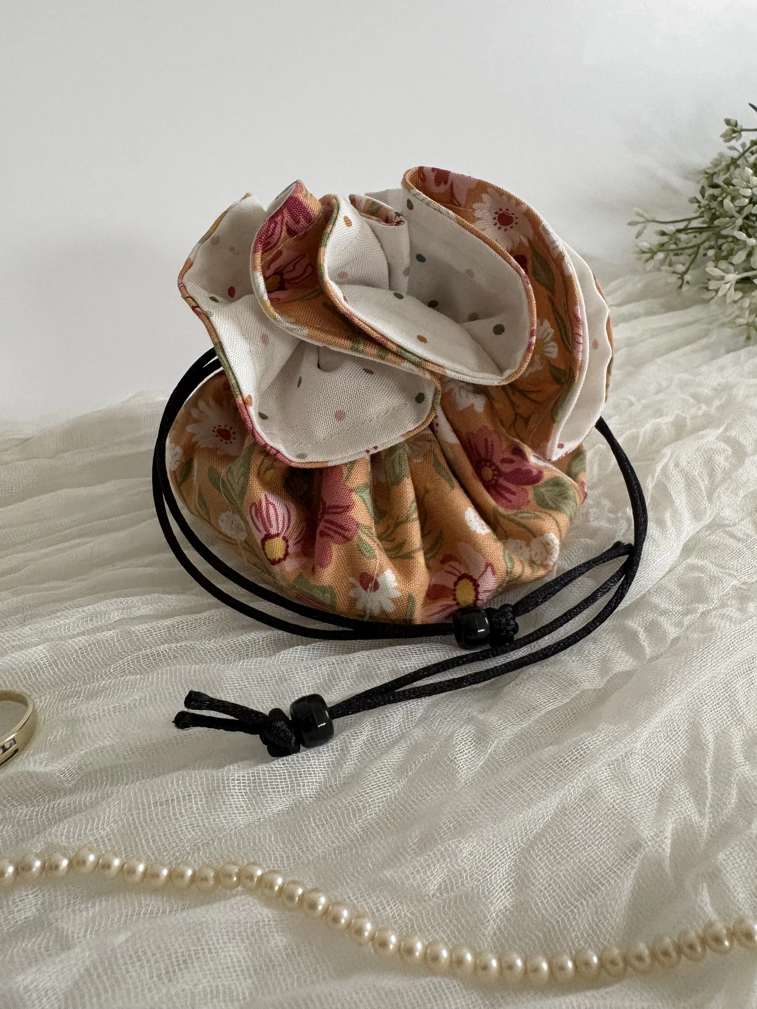 A floral fabric scrunchie resting on a white textured surface, with a string of pearls and a beaded bracelet nearby.