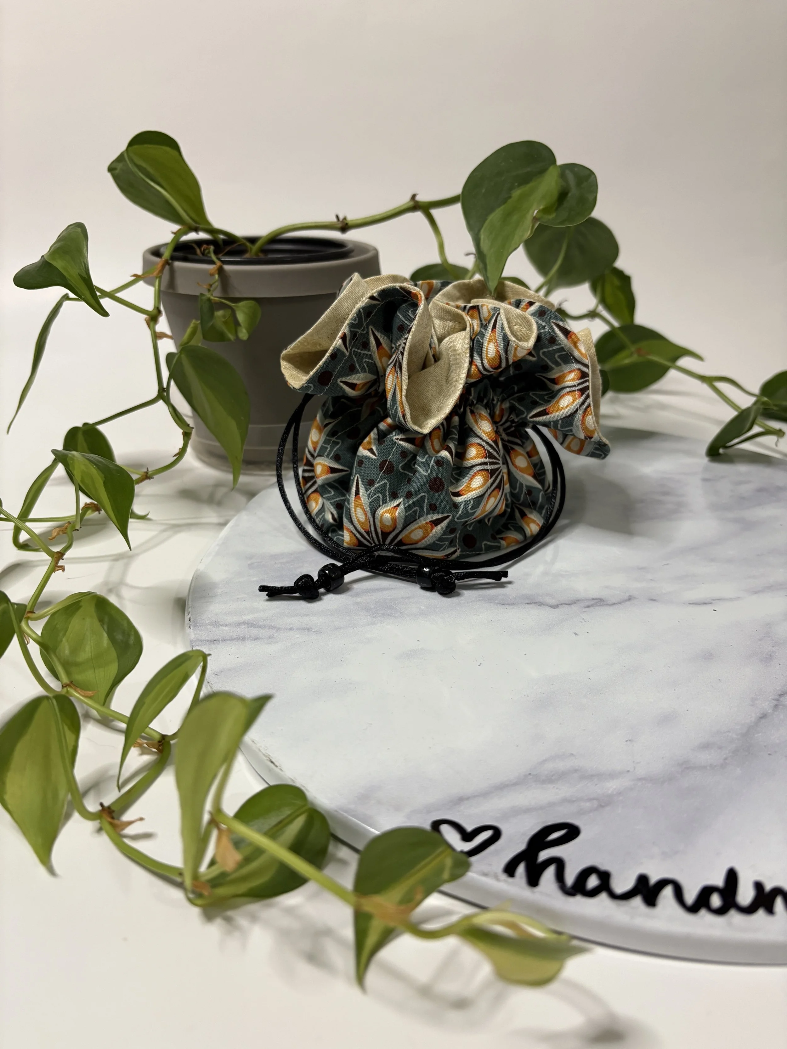A potted green plant with trailing vines and heart-shaped leaves next to a round, white decorated object with a black handwritten message and a small heart symbol on it.