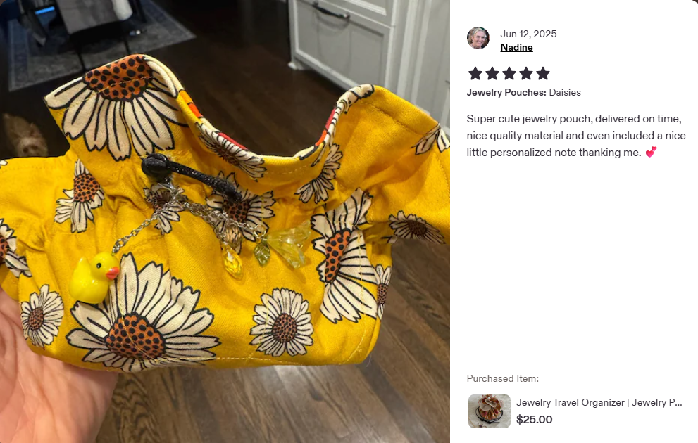 Yellow floral jewelry pouch with daisies design, featuring jewelry items including a gold chain with charms and a yellow rubber duck keychain, held in a person's hand in a home setting.