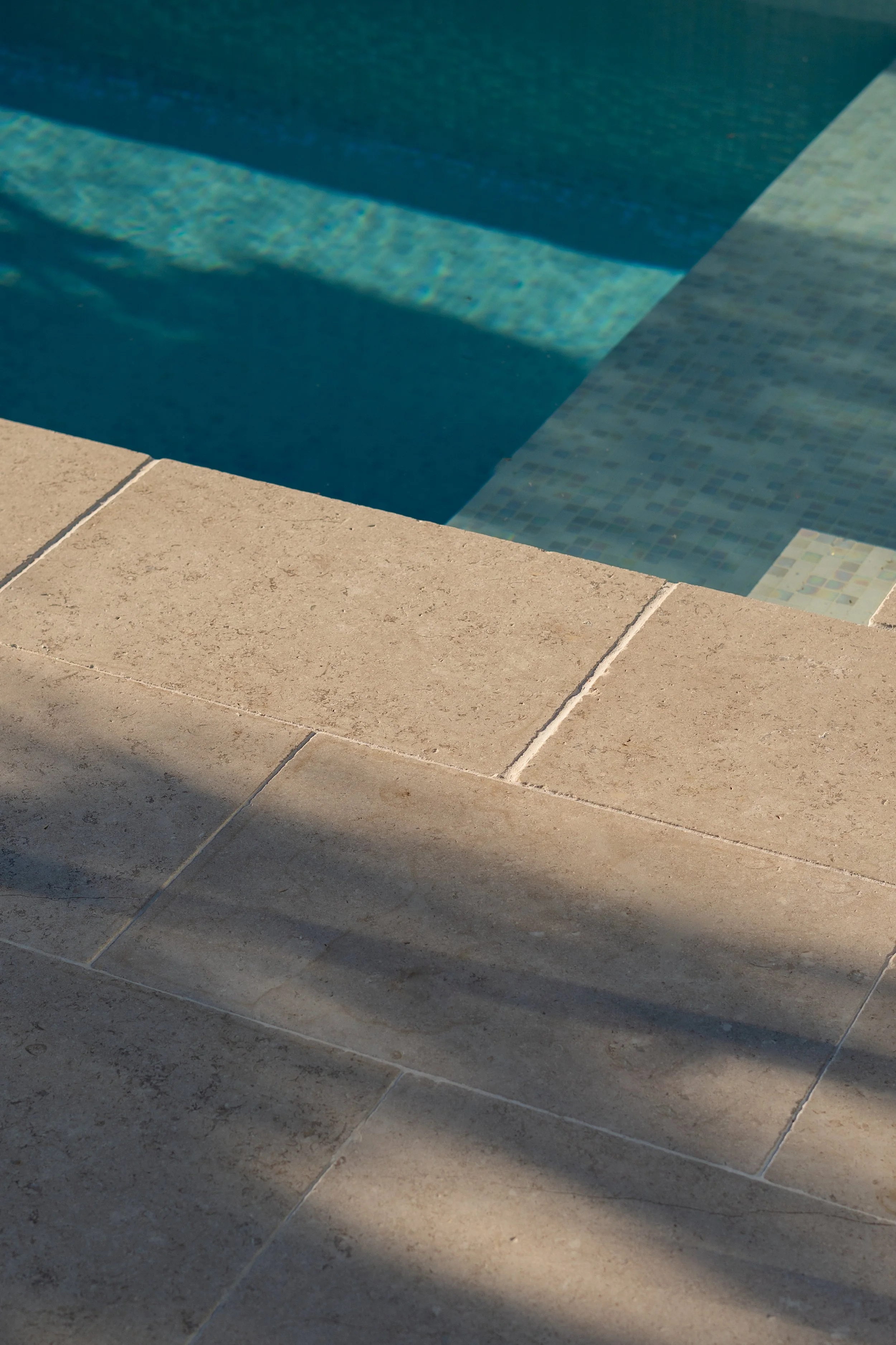 Natural stone pool coping and paving beside a custom swimming pool in a Central Coast landscape design.
