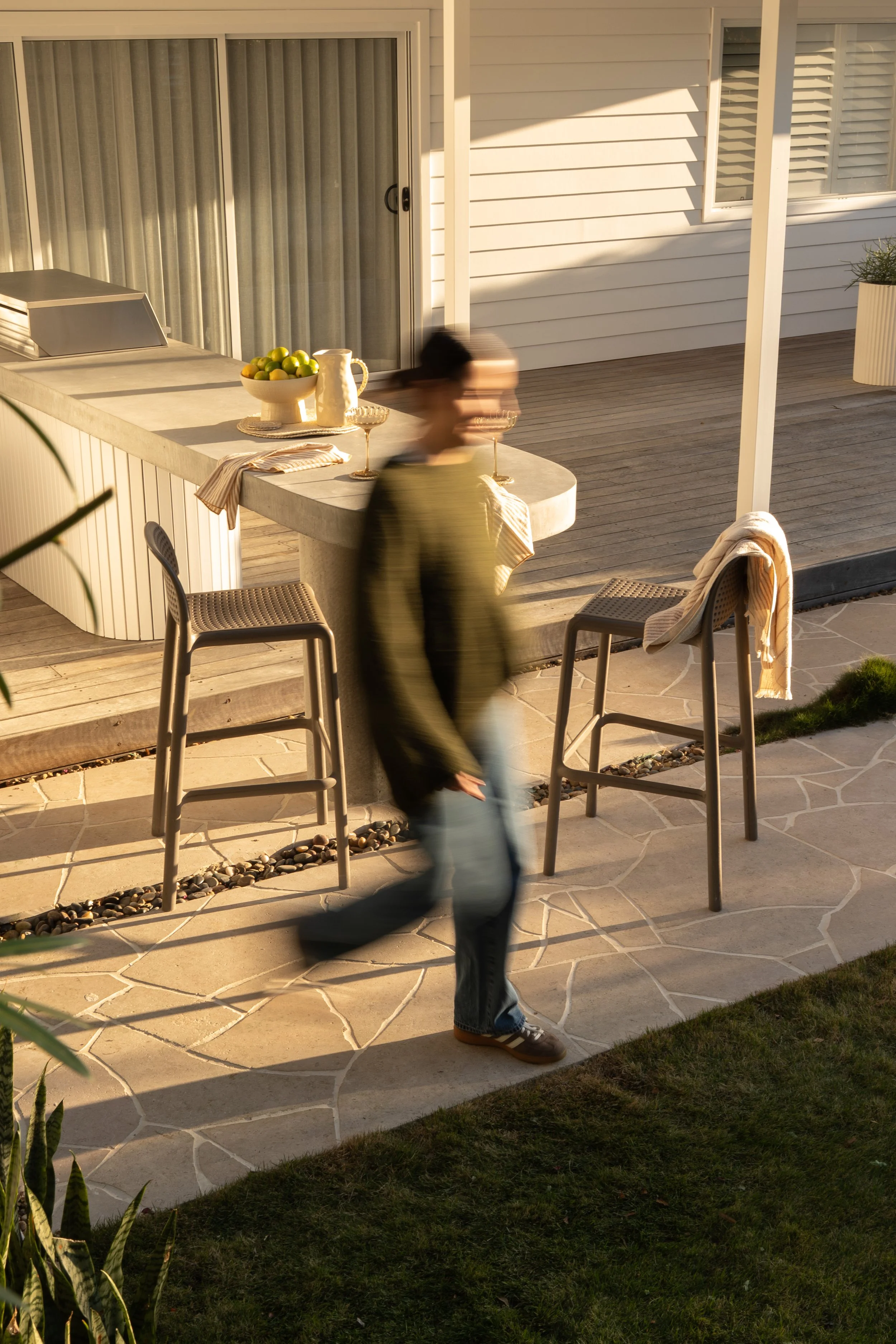 Person walking through a compact Wamberal outdoor living area with a custom cooking bench and natural stone crazy paving.
