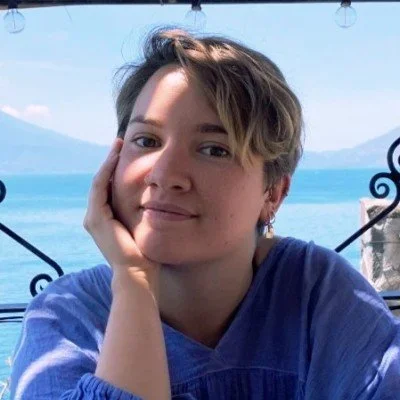 Woman with short hair smiling and resting her face on her hand at an outdoor lakeside location