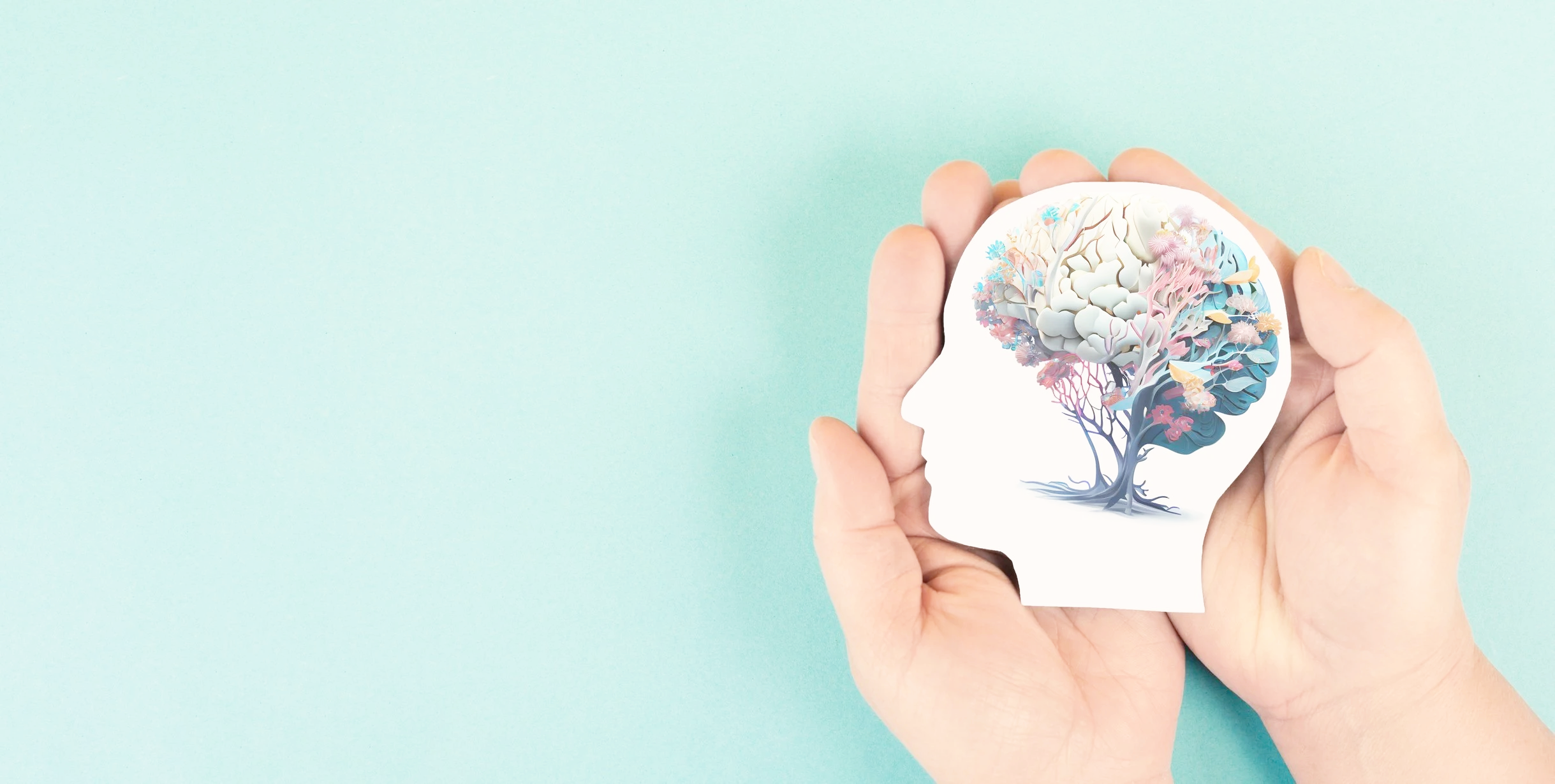 Two hands holding a paper cutout of a human head silhouette with a colorful brain and tree illustration inside representing Mindful Mind counselling work.
