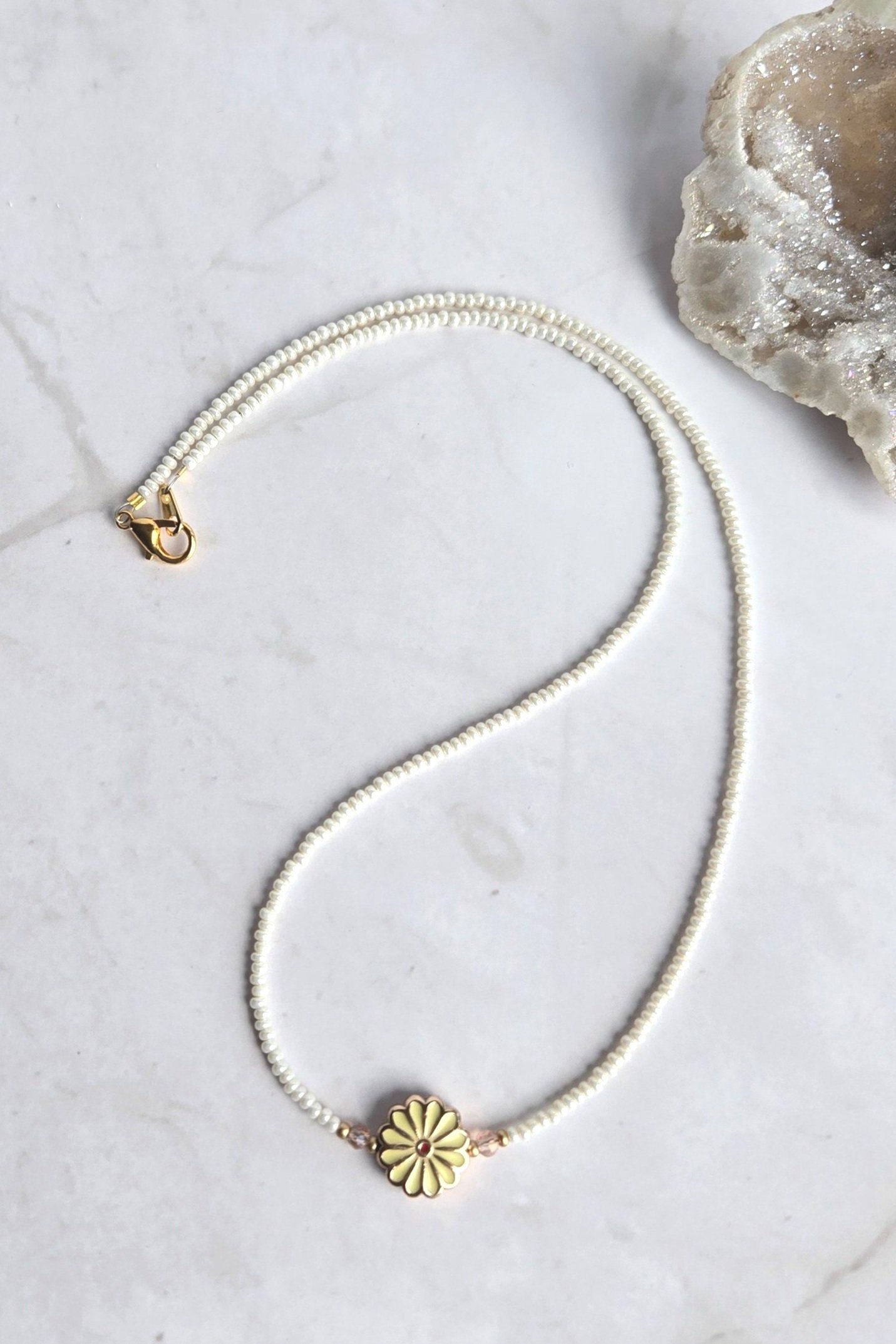 Hand beaded necklace featuring a soft yellow daisy enamel bead, accented by gold seed beads and crystal briolette beads.