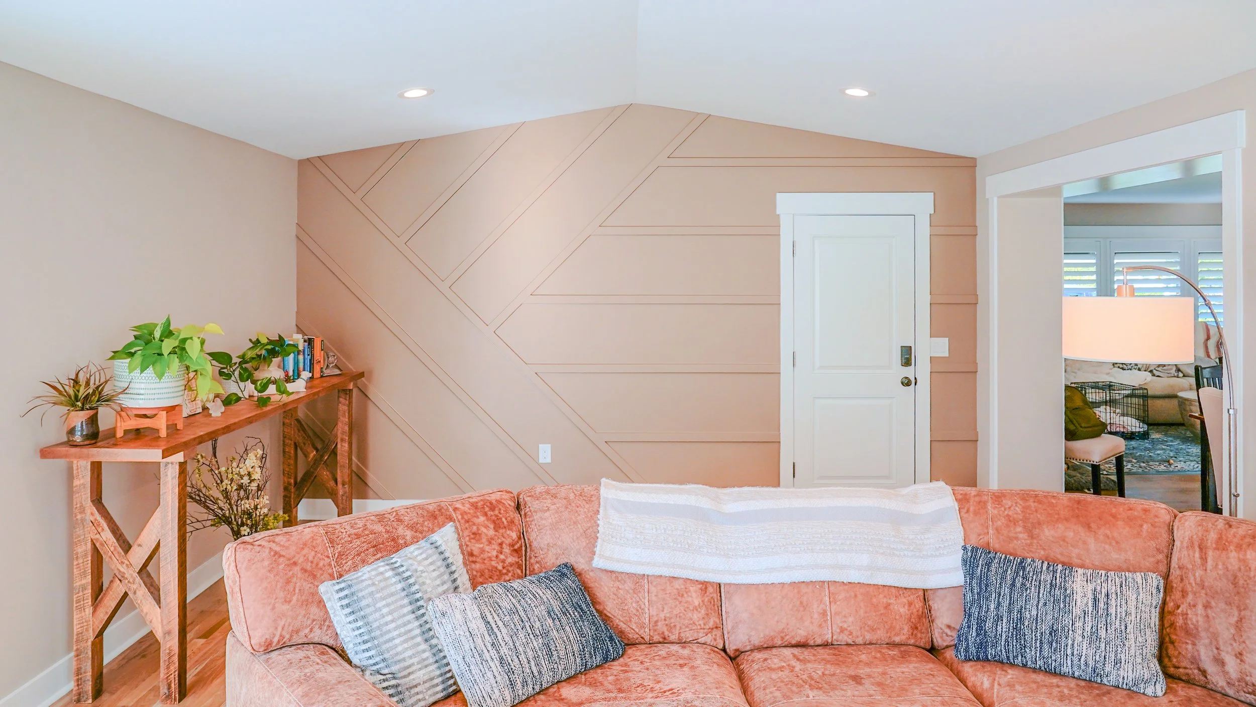 Accent wall with a brown couch in front of it and a decorative table on the side with a door to the garage