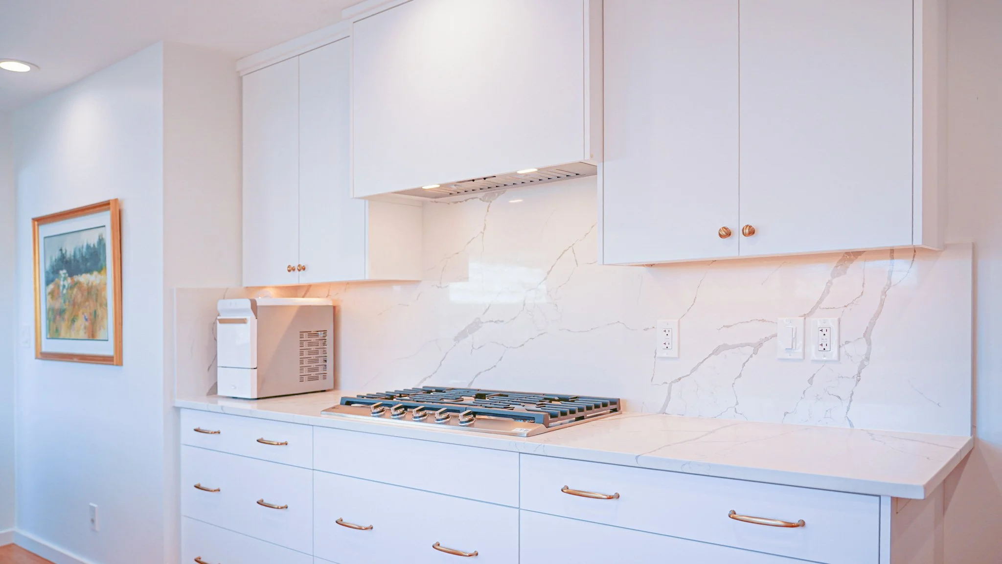 White cabinetry with bronze pulls, built-in cooktop, and granite backsplash wall
