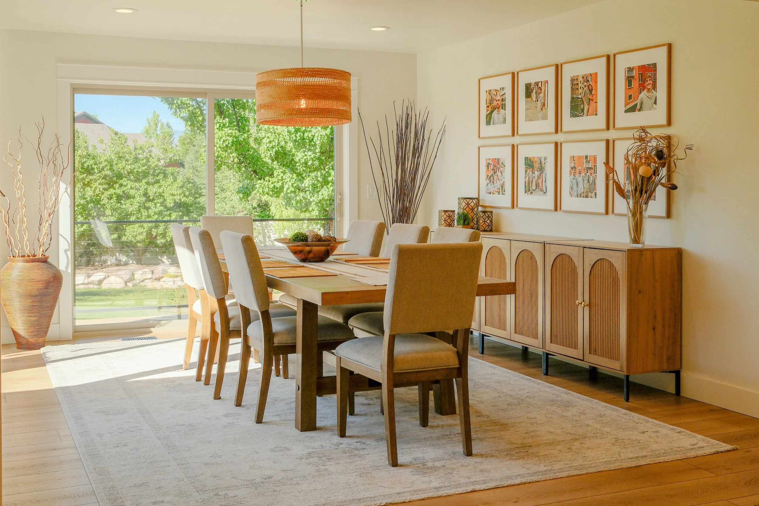 Bright living room with large windows, two black leather couches, a flat-screen TV mounted above a white fireplace, light-colored built-in shelves, and a colorful area rug.