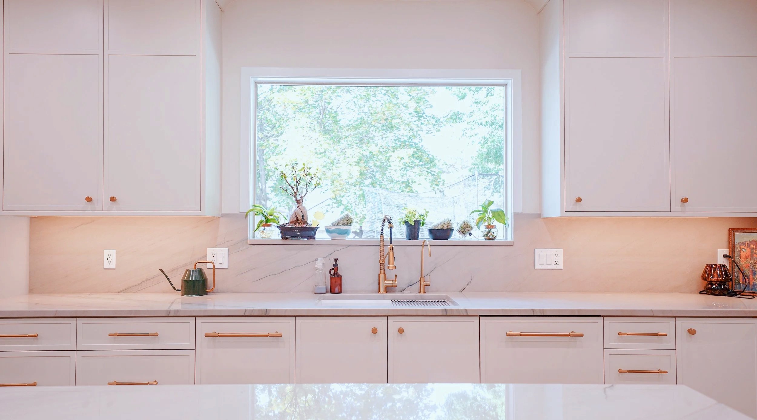 A modern kitchen with white cabinets, stainless steel appliances, a gas stove, a range hood, and a sink near a window